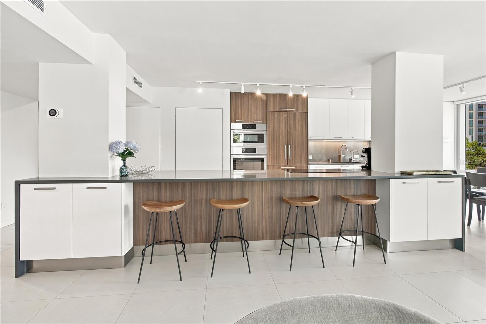 Modern kitchen with a long wood-front island, four bar stools, and stainless-steel appliances.
