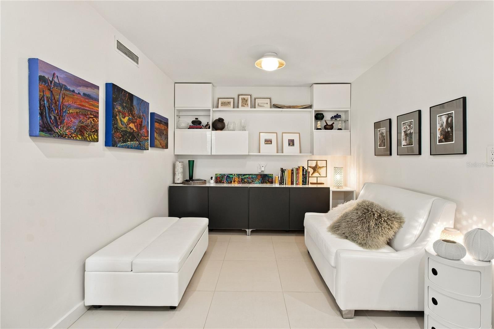 Furnished sitting room with white leather sofas, built-in shelves, and colorful artwork.