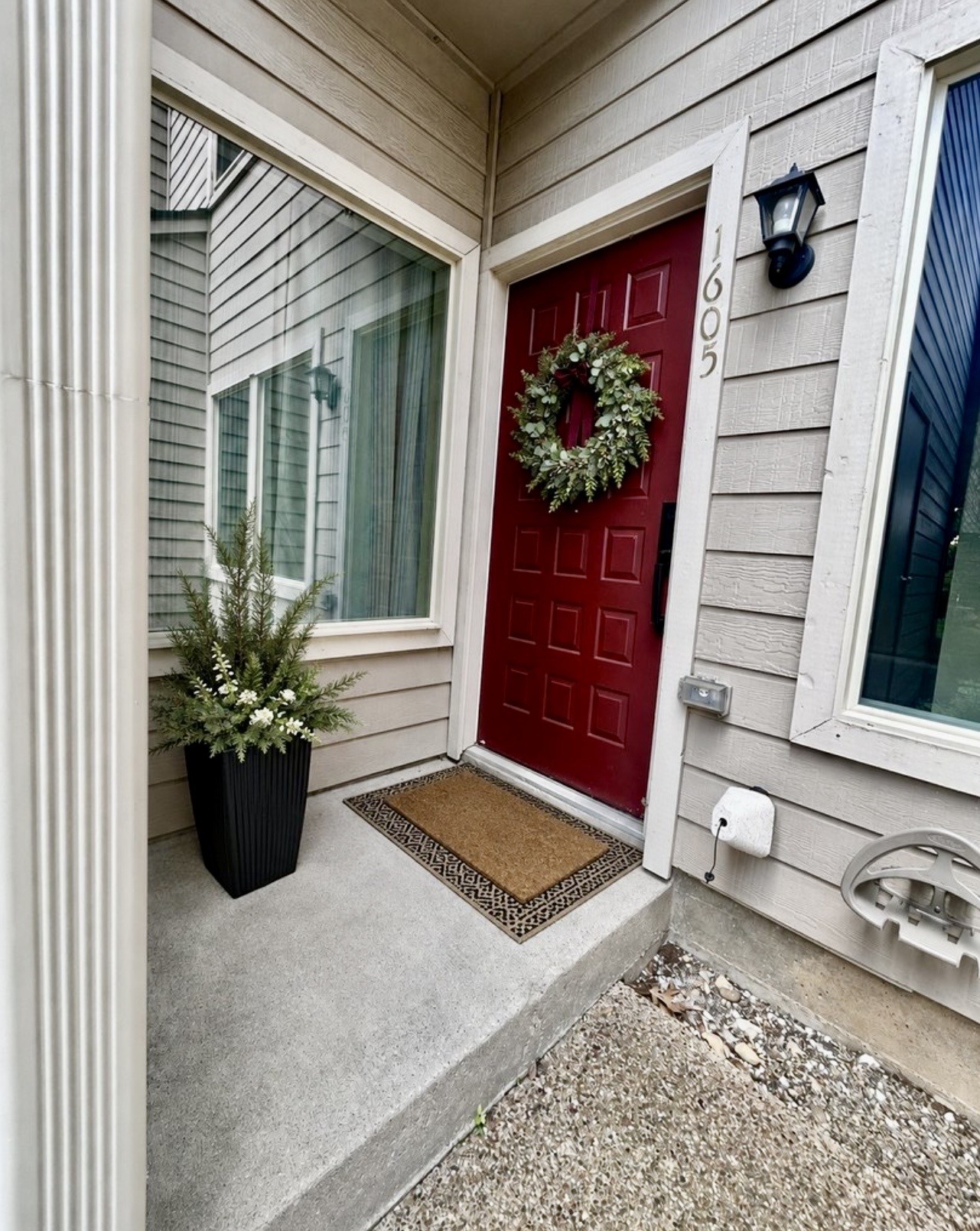 Townhouse entry with a red door, wreath, and potted flowers beside the number 1605.