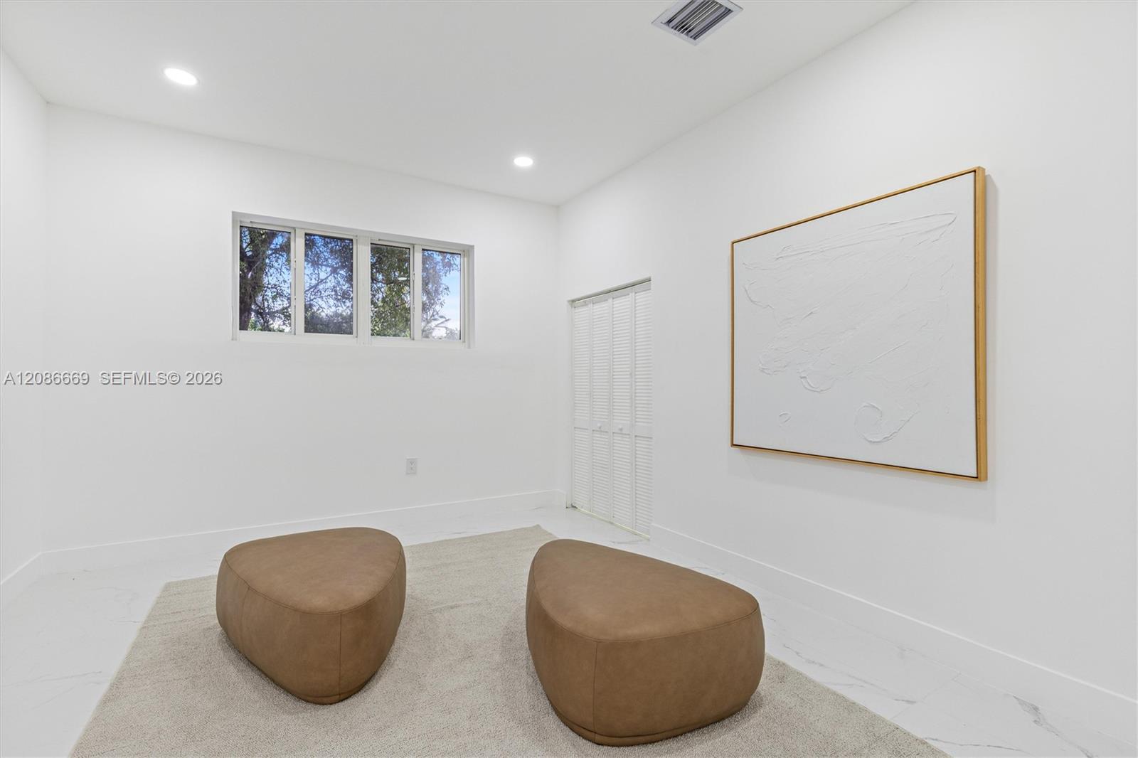 Minimalist sitting room with two tan ottomans, a pale rug, and large neutral abstract art.