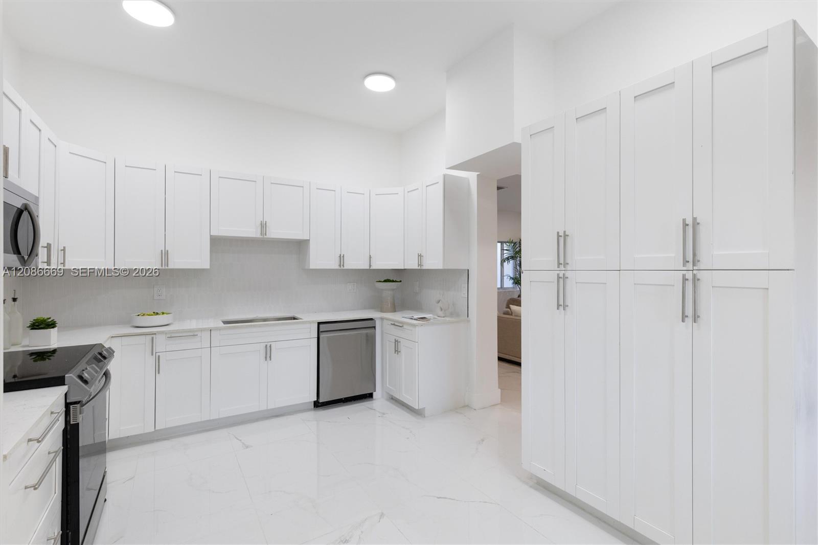 Bright white kitchen with tall pantry cabinets, marble-look surfaces, and stainless steel appliances.