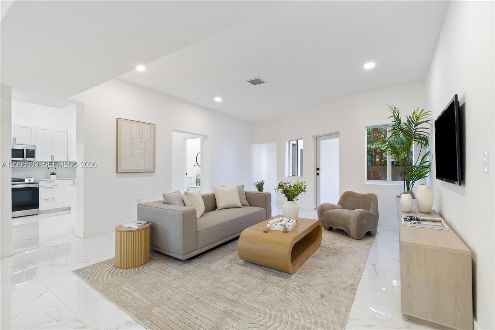 Staged living room with a gray sofa, sculptural wood coffee table, and open kitchen.