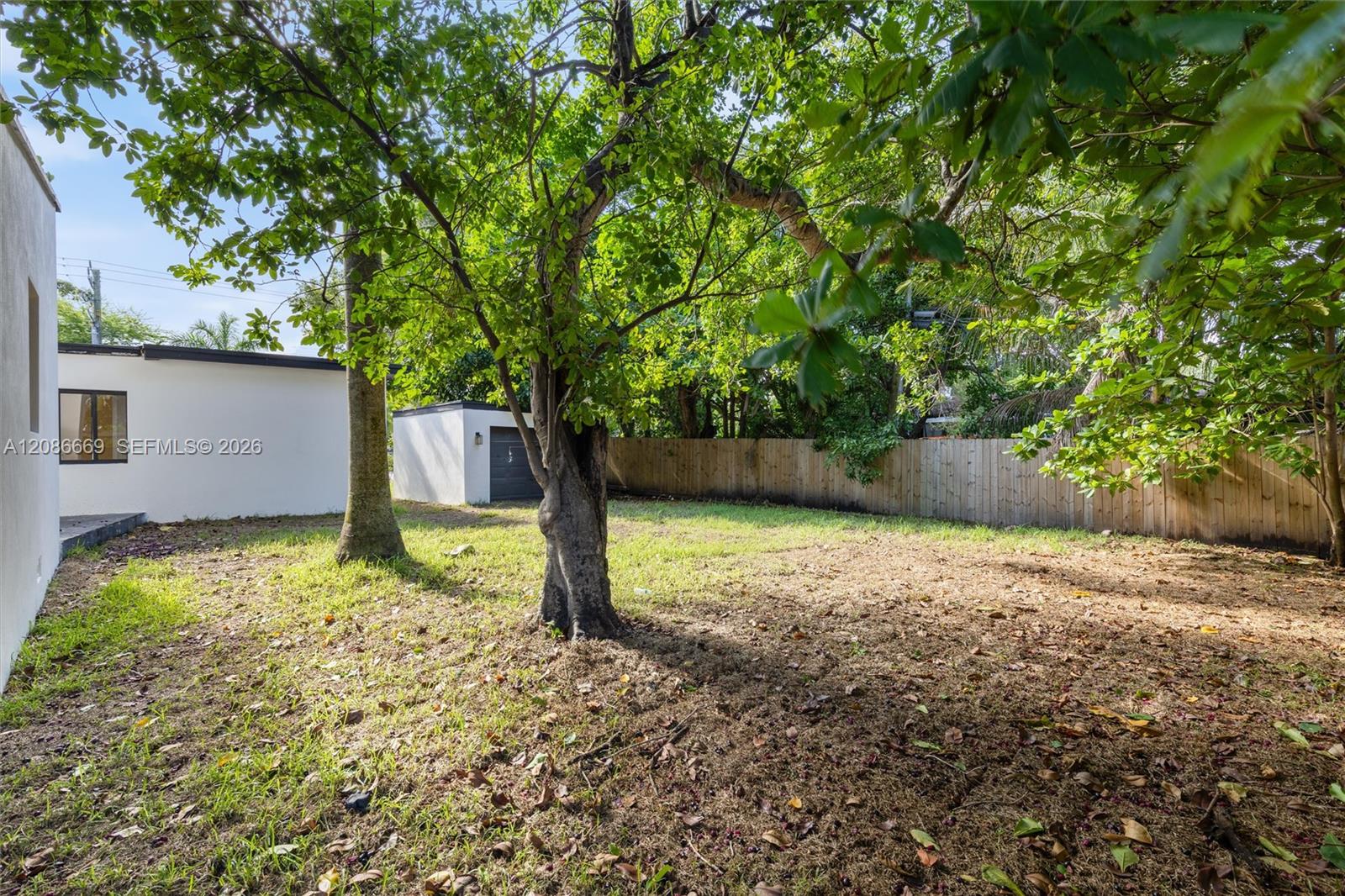 Shaded backyard with mature trees, a wooden fence, and a small white outbuilding.