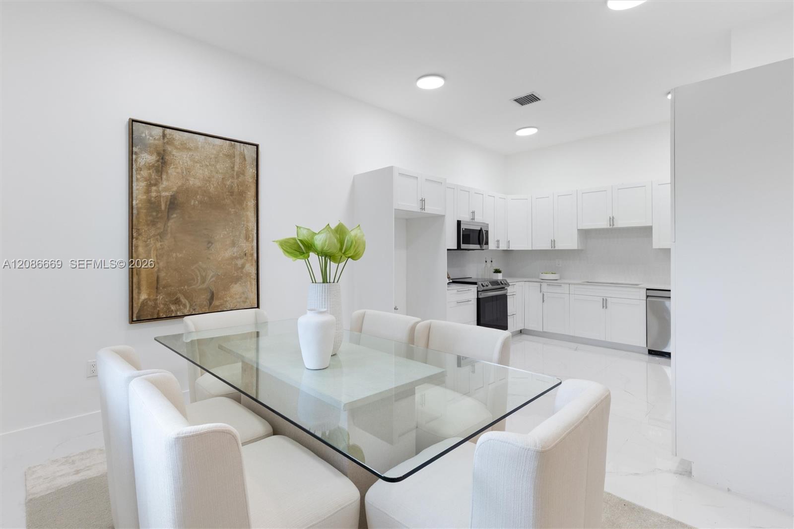 Open-plan kitchen and dining area with white cabinets and a glass table.
