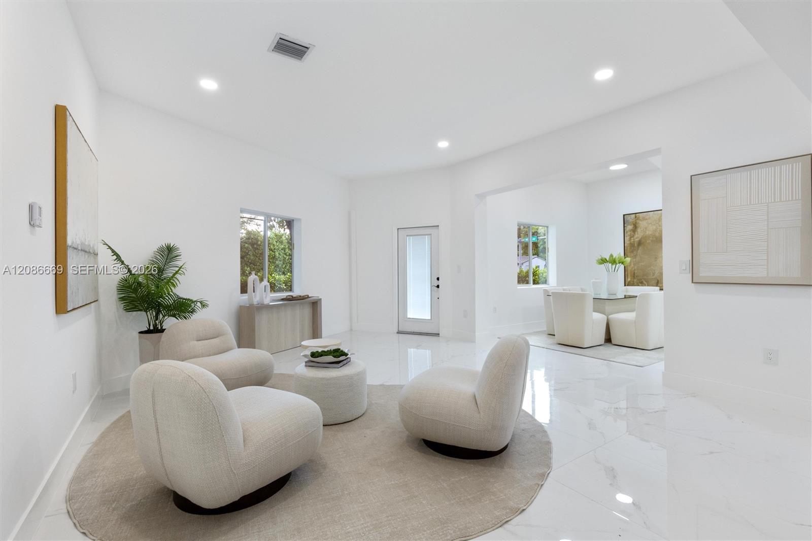 Staged living room with rounded cream chairs, a low table, and an adjoining dining area.