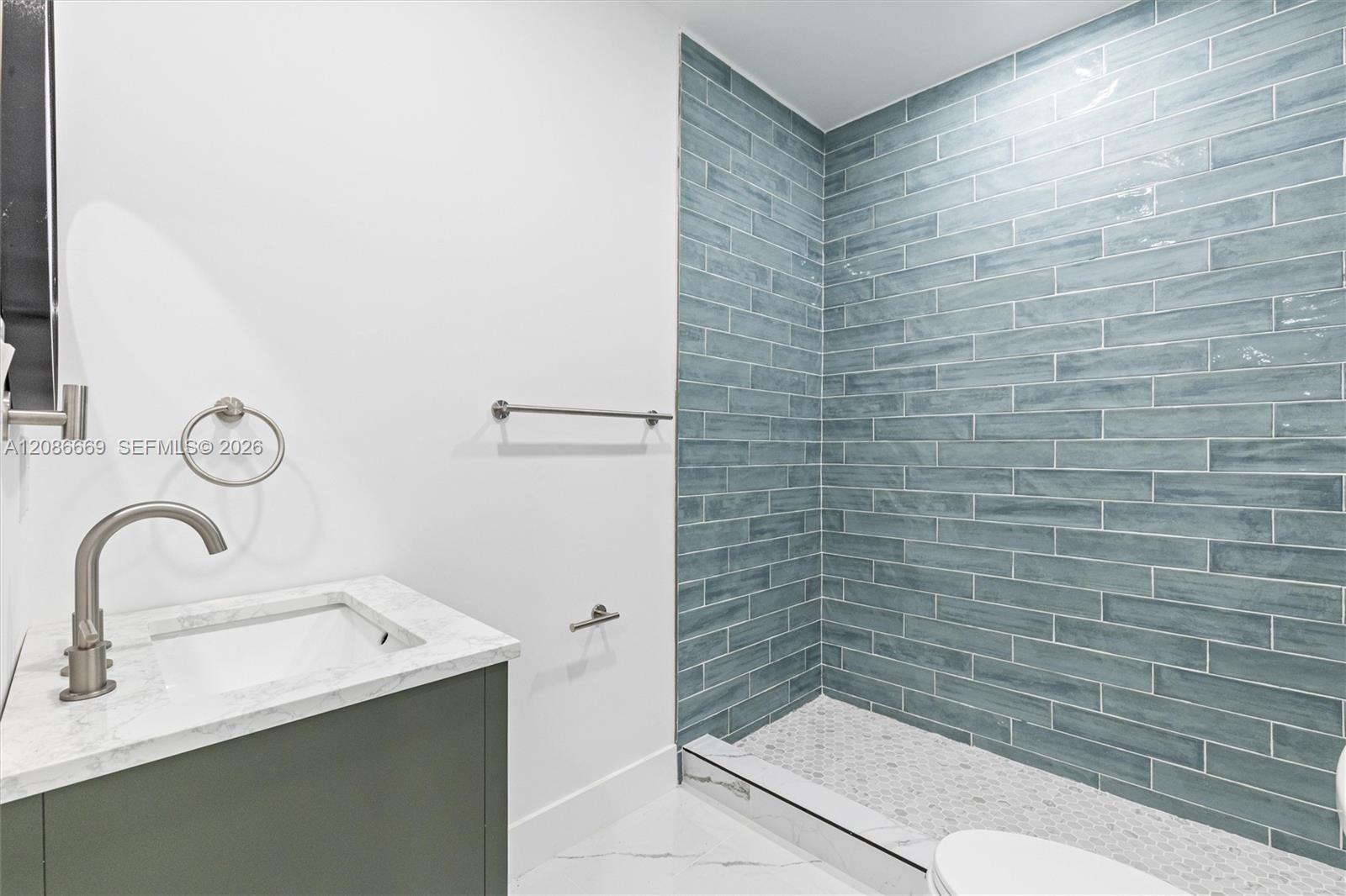 Bathroom with blue-gray tiled walk-in shower and dark green marble-topped vanity.