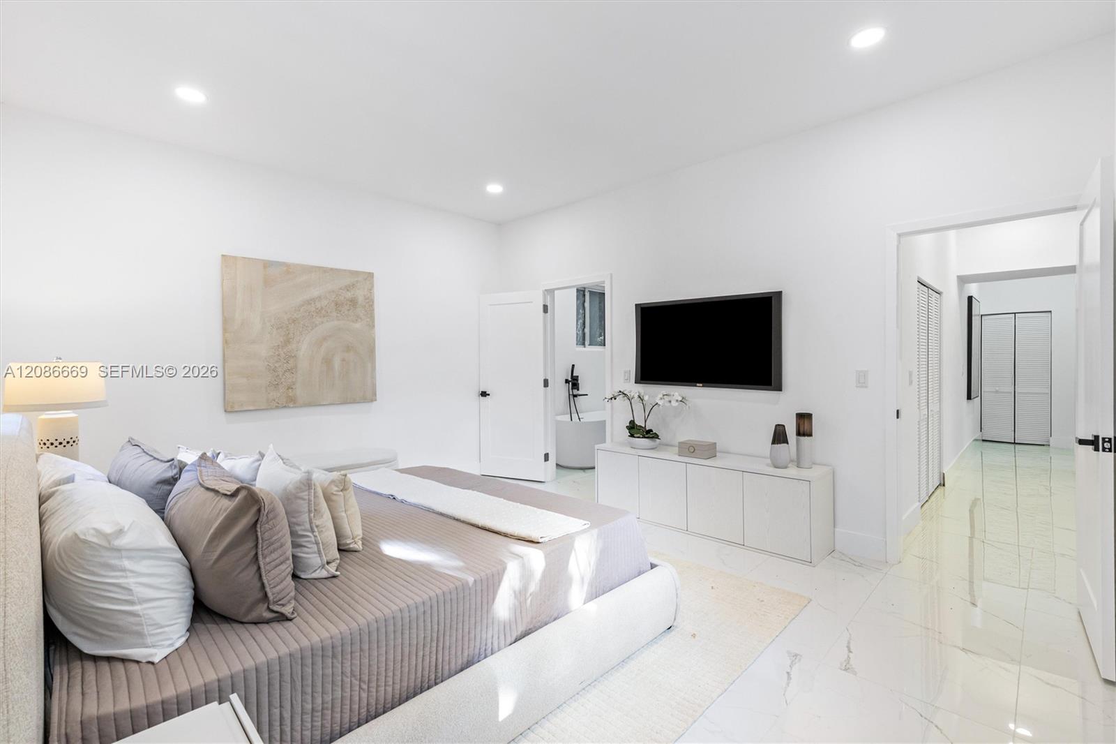 Bright modern bedroom with a low upholstered bed, neutral bedding, and wall-mounted television.