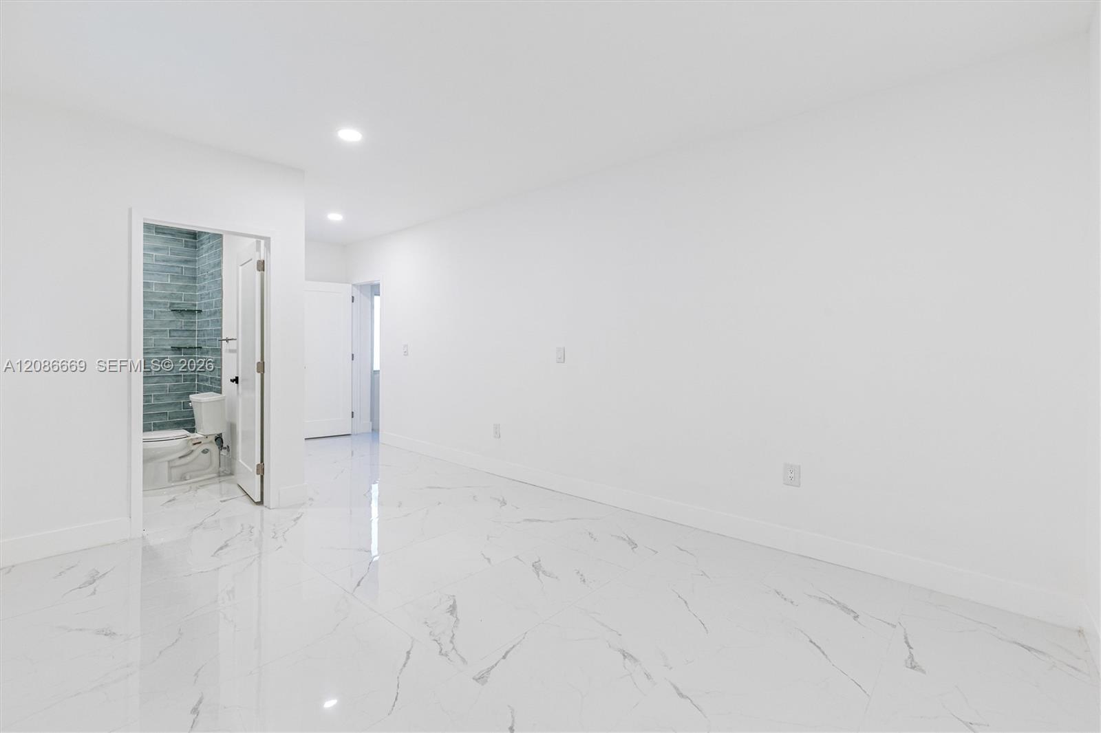 Vacant interior room with glossy veined tile floors and an open doorway to a blue-green tiled bathroom.