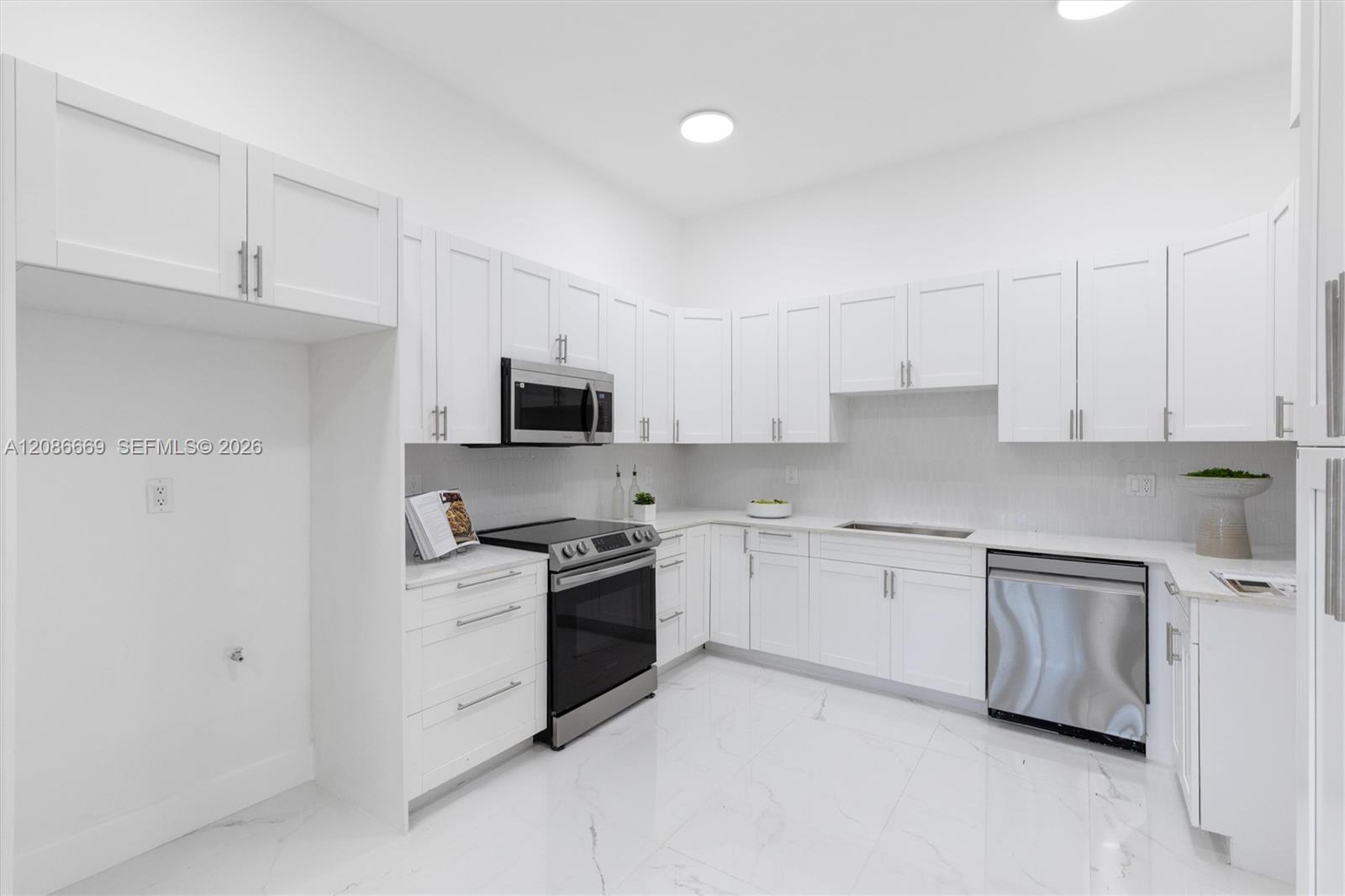 Modern white kitchen with shaker cabinets, marble-look floors, stainless dishwasher, and dark range.