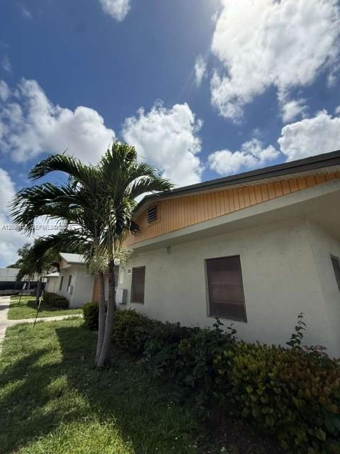 Low-rise stucco property with a palm tree, shrubs, and grassy lawn.