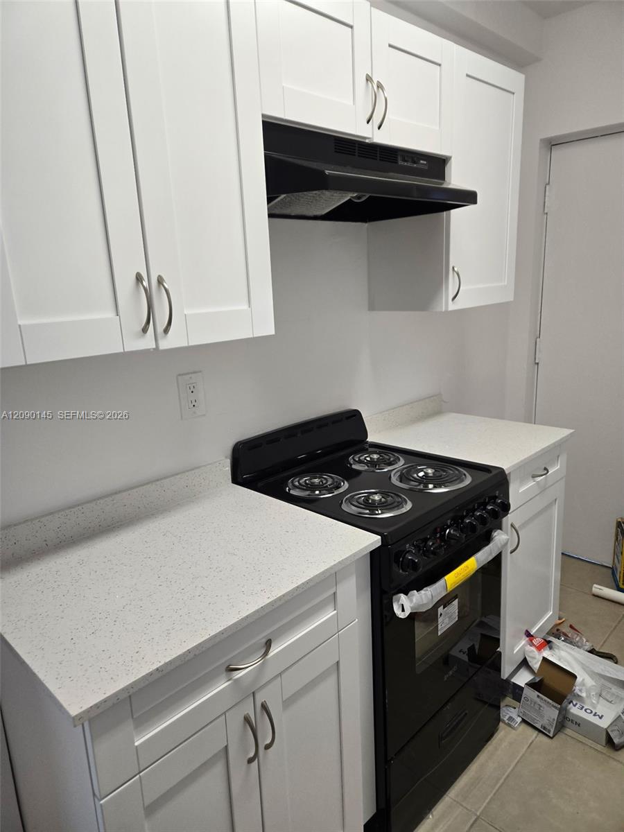 Kitchen with white cabinets and counters, a black coil-top electric range, and renovation supplies on the floor.