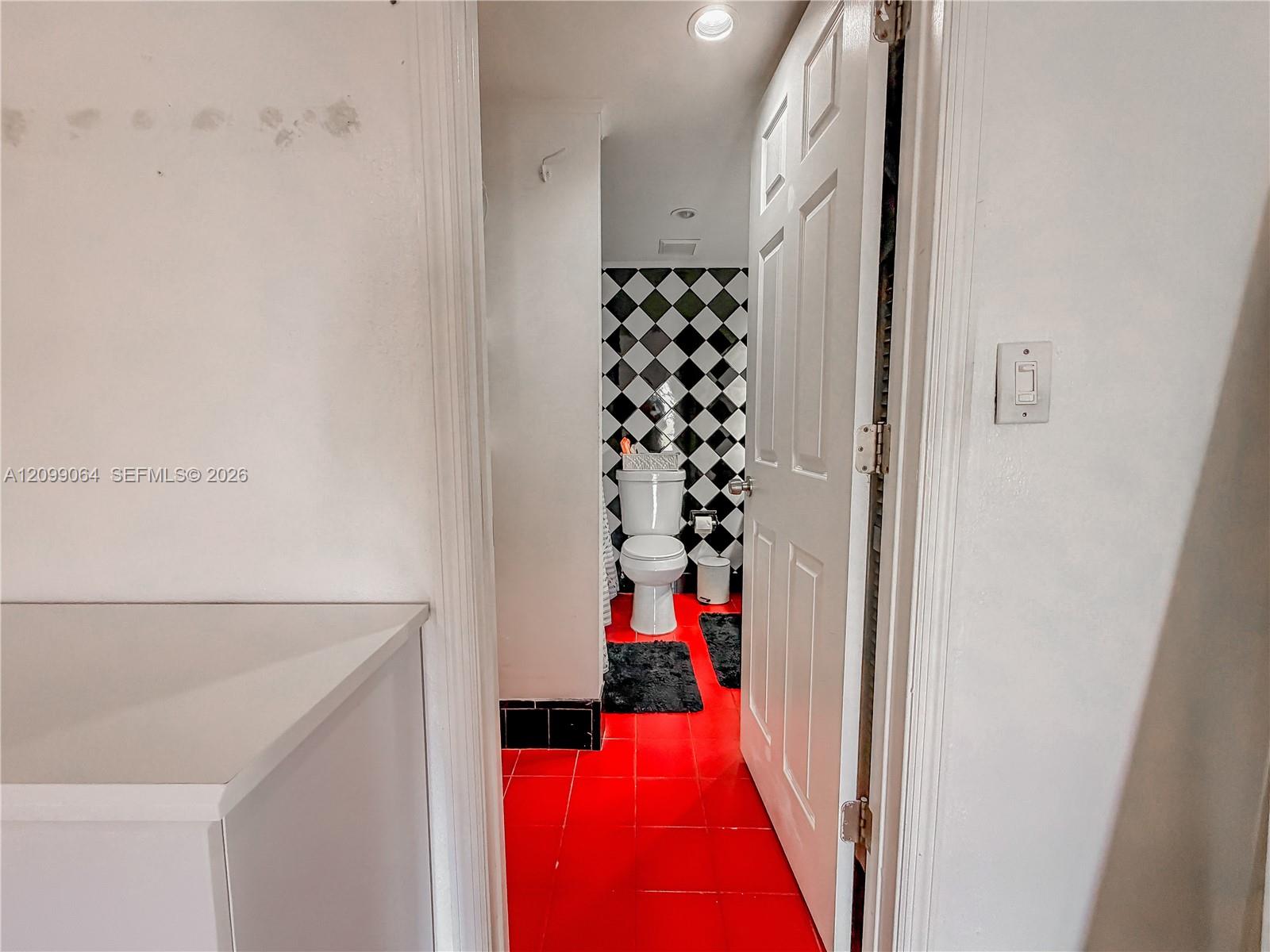 Bathroom with a white toilet, black-and-white diamond tile, and vivid red flooring.