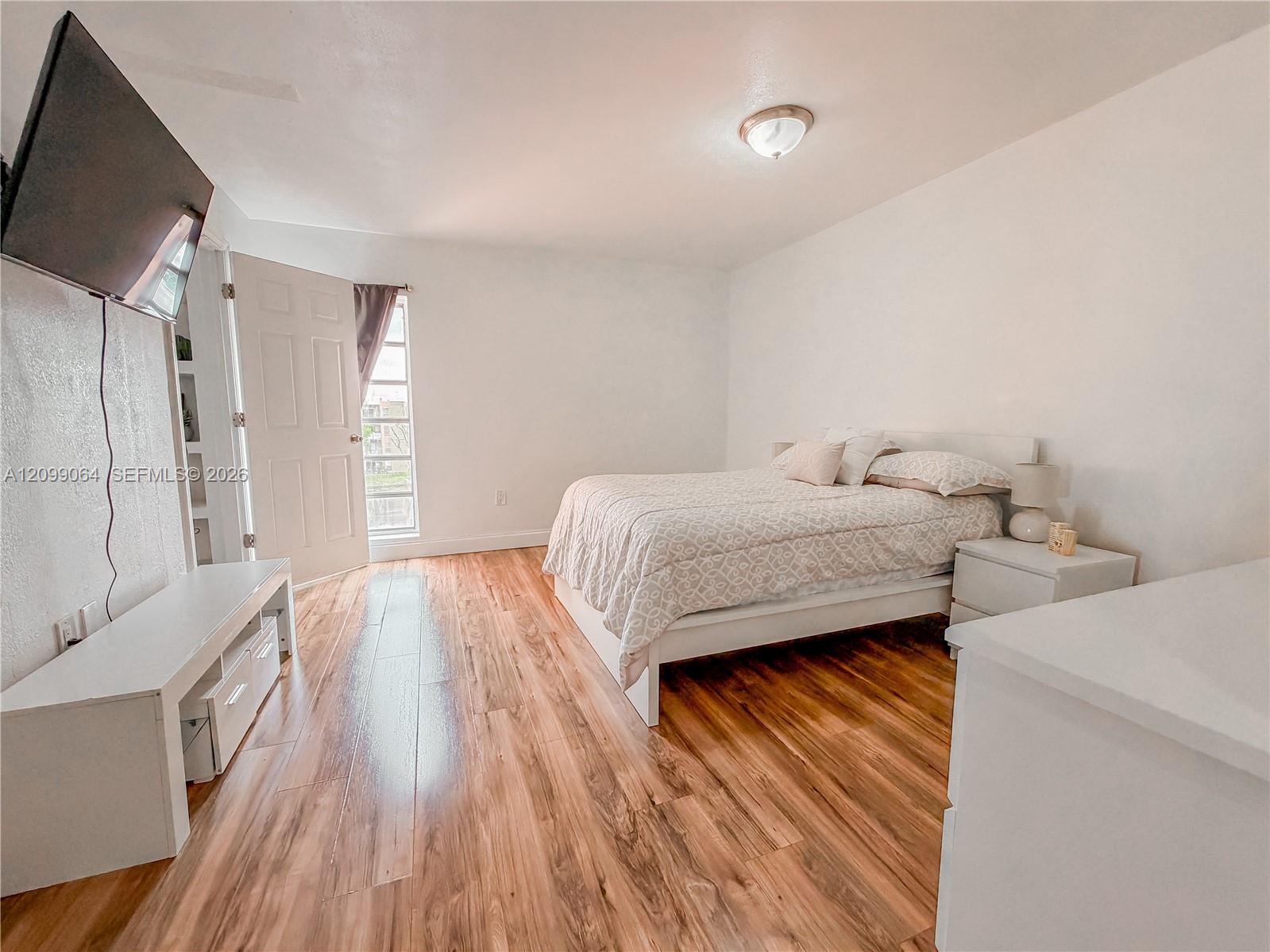 Bedroom with a patterned bedspread, warm wood-look floors, and a wall-mounted television.