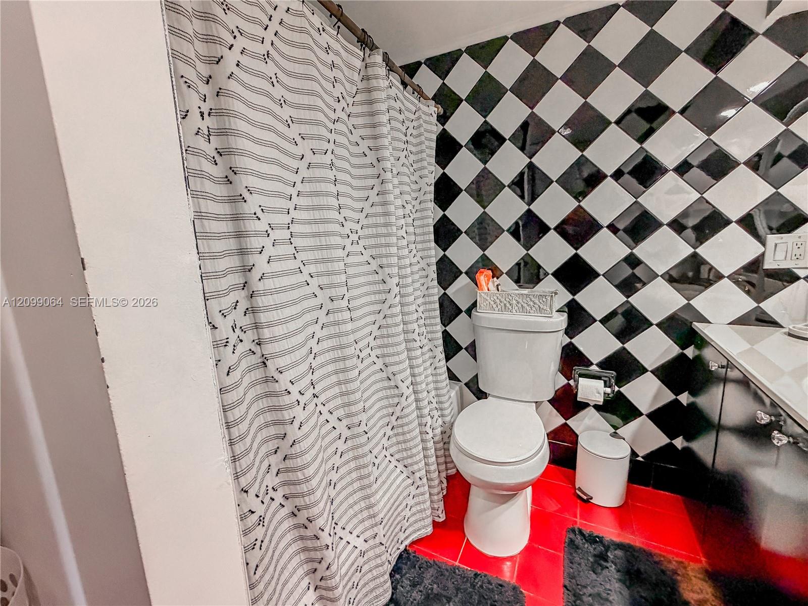 Bathroom with checkerboard walls, red tile flooring, and a patterned shower curtain.