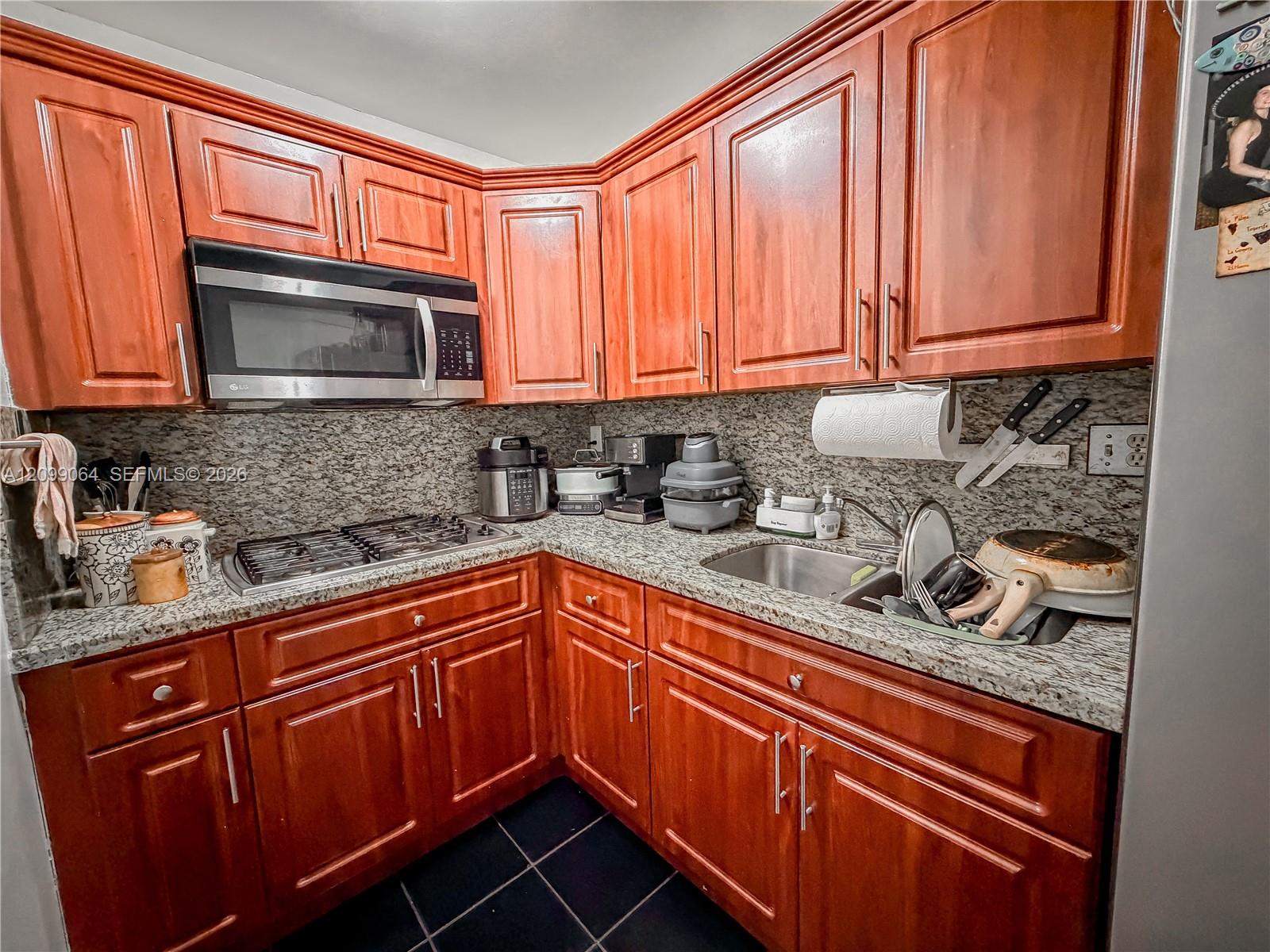 Kitchen with reddish wood cabinets, granite counters, stainless microwave, gas cooktop, and sink.