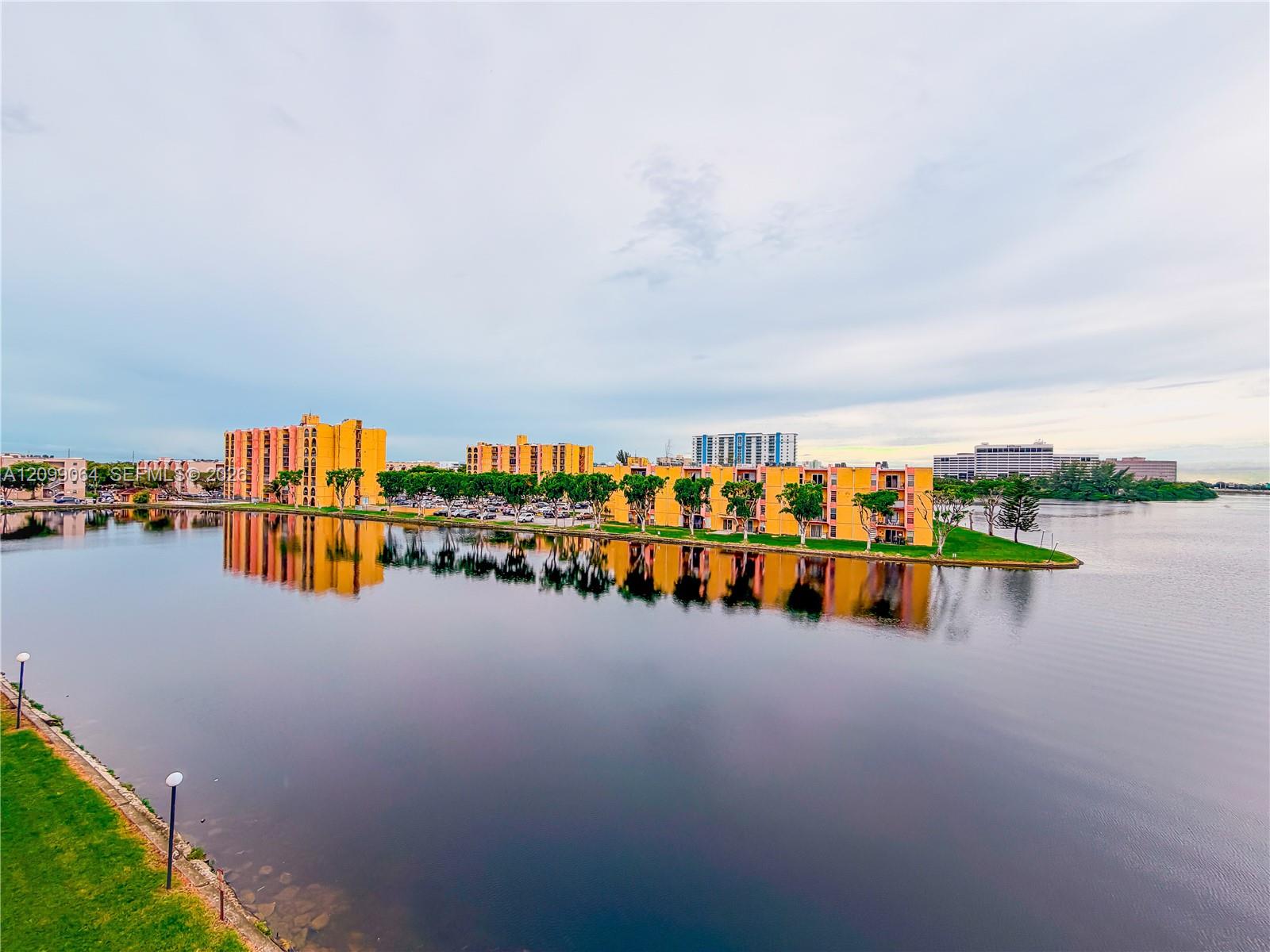 Waterfront apartment buildings reflected in a calm lagoon beneath a cloudy sky.