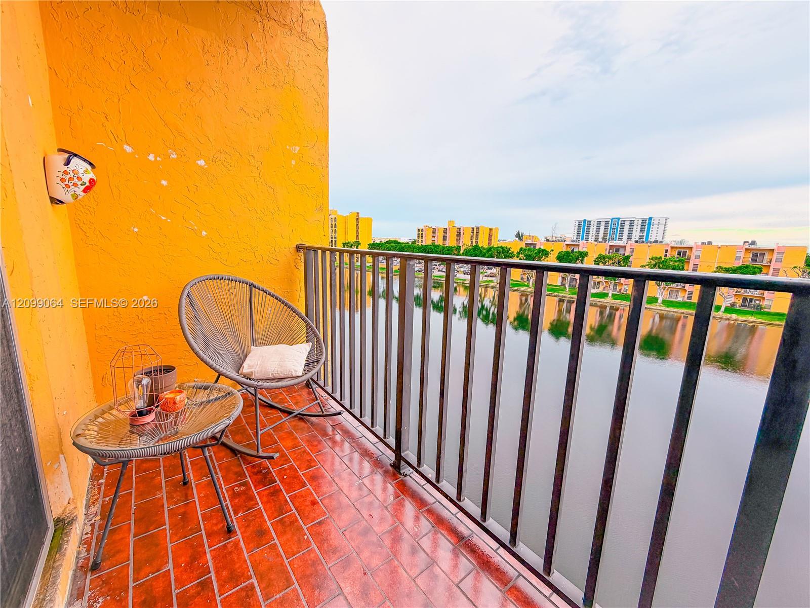 Furnished balcony with woven chairs overlooking a canal and neighboring apartments.
