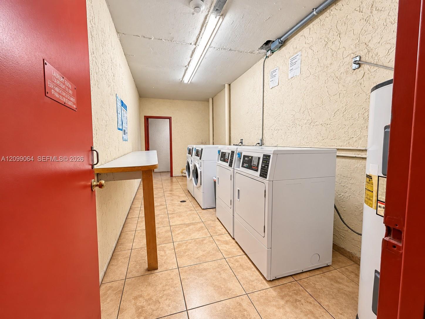 Shared laundry room with rows of white washers and dryers and a red doorway.