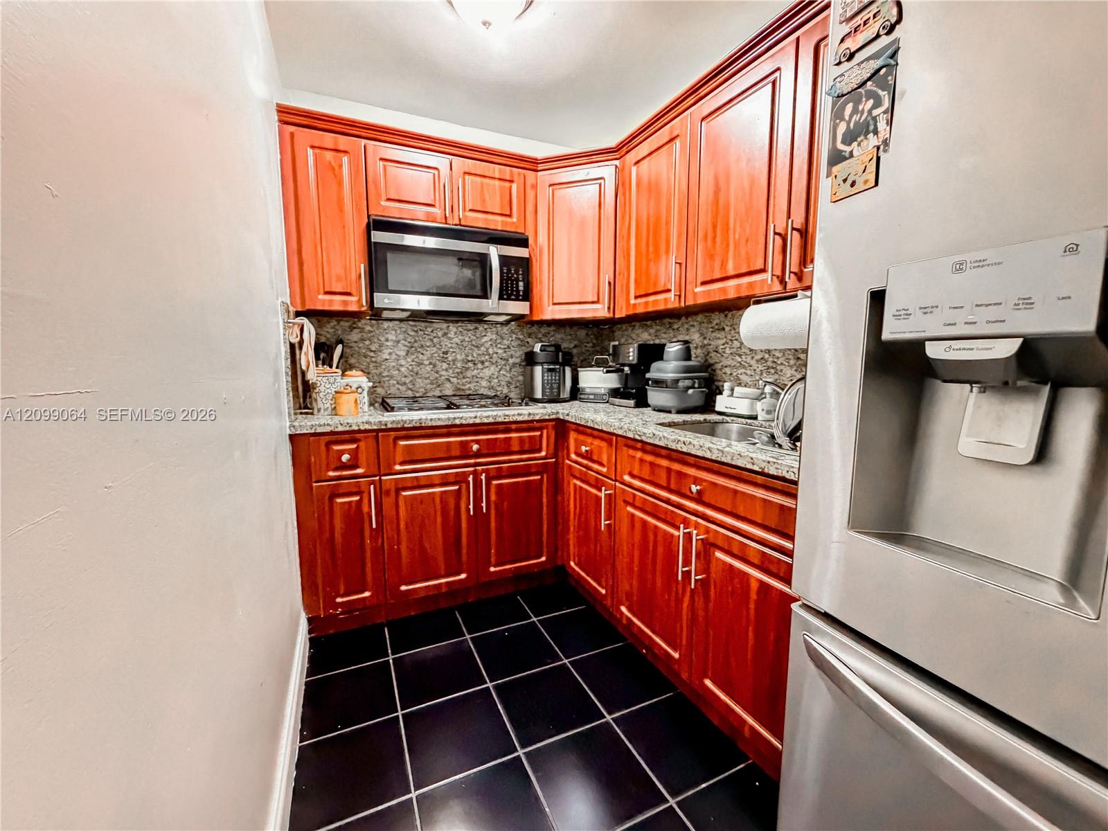 Kitchen with reddish wood cabinets, granite counters, stainless steel appliances, and black tile flooring.