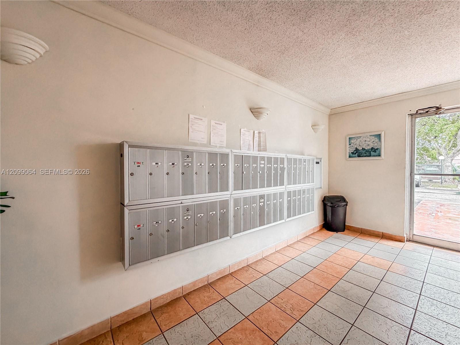 Building mailroom with rows of metal mailboxes beside a glass entrance door.