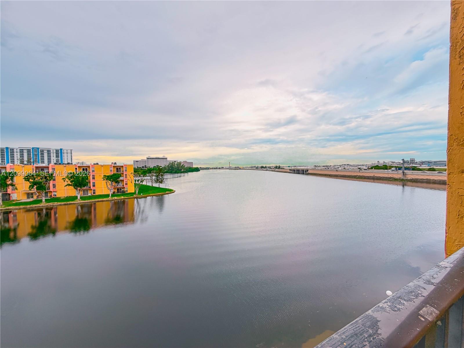 Waterway view from a balcony, framed by a yellow wall and railing, with colorful apartments along the shore.