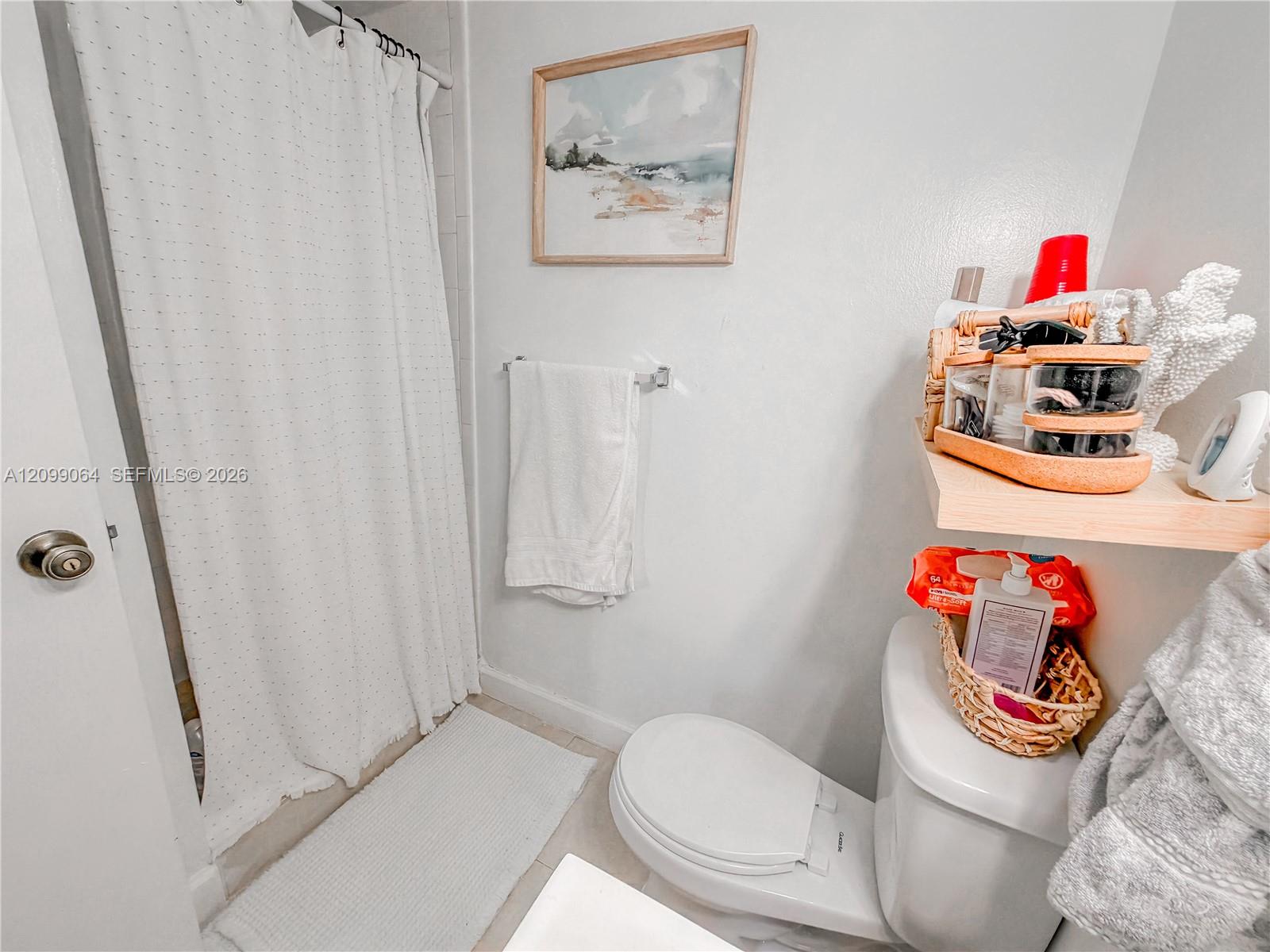 Bathroom with a dotted shower curtain, white towels, and toiletries arranged beside the toilet.