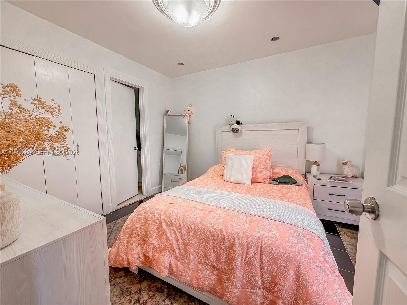 Bedroom with coral patterned bedding, pale furniture, and built-in closet doors.