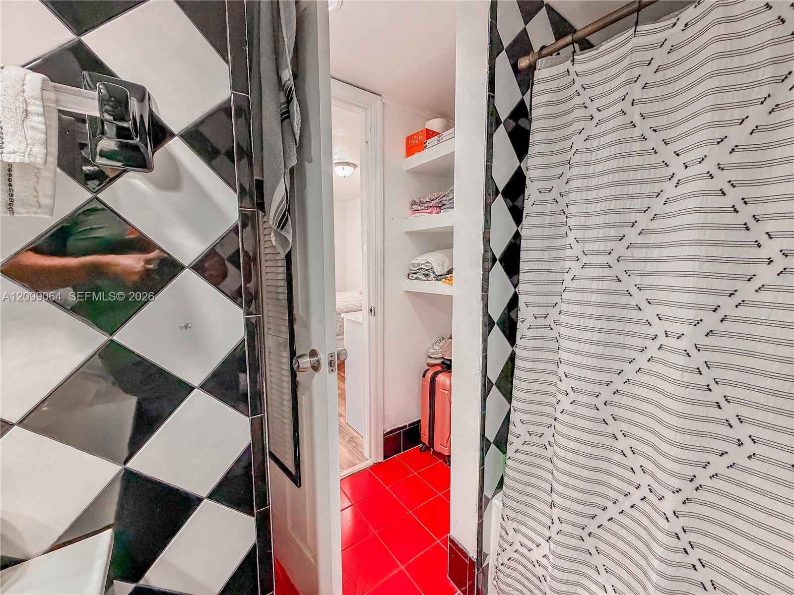 Bathroom with black-and-white diamond tile, a patterned shower curtain, and vivid red floor tiles.