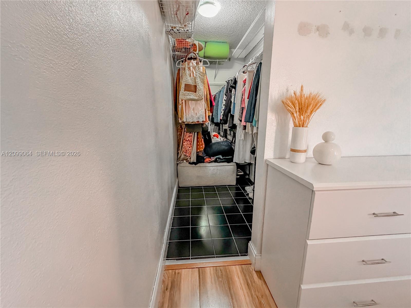 Walk-in closet with hanging clothes, overhead wire shelves, a bench, and dark tile flooring.