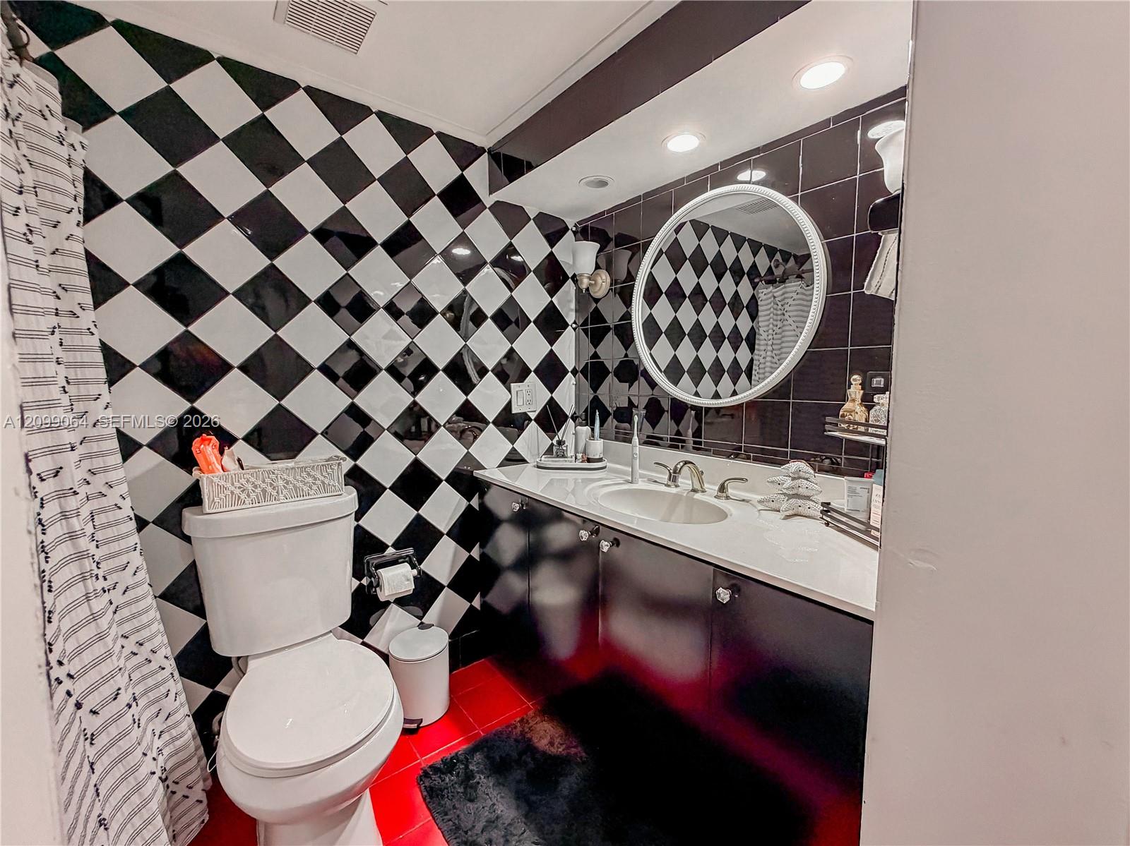 Bathroom with checkerboard tile walls, a dark double-sink vanity, round mirror, and red floor tiles.