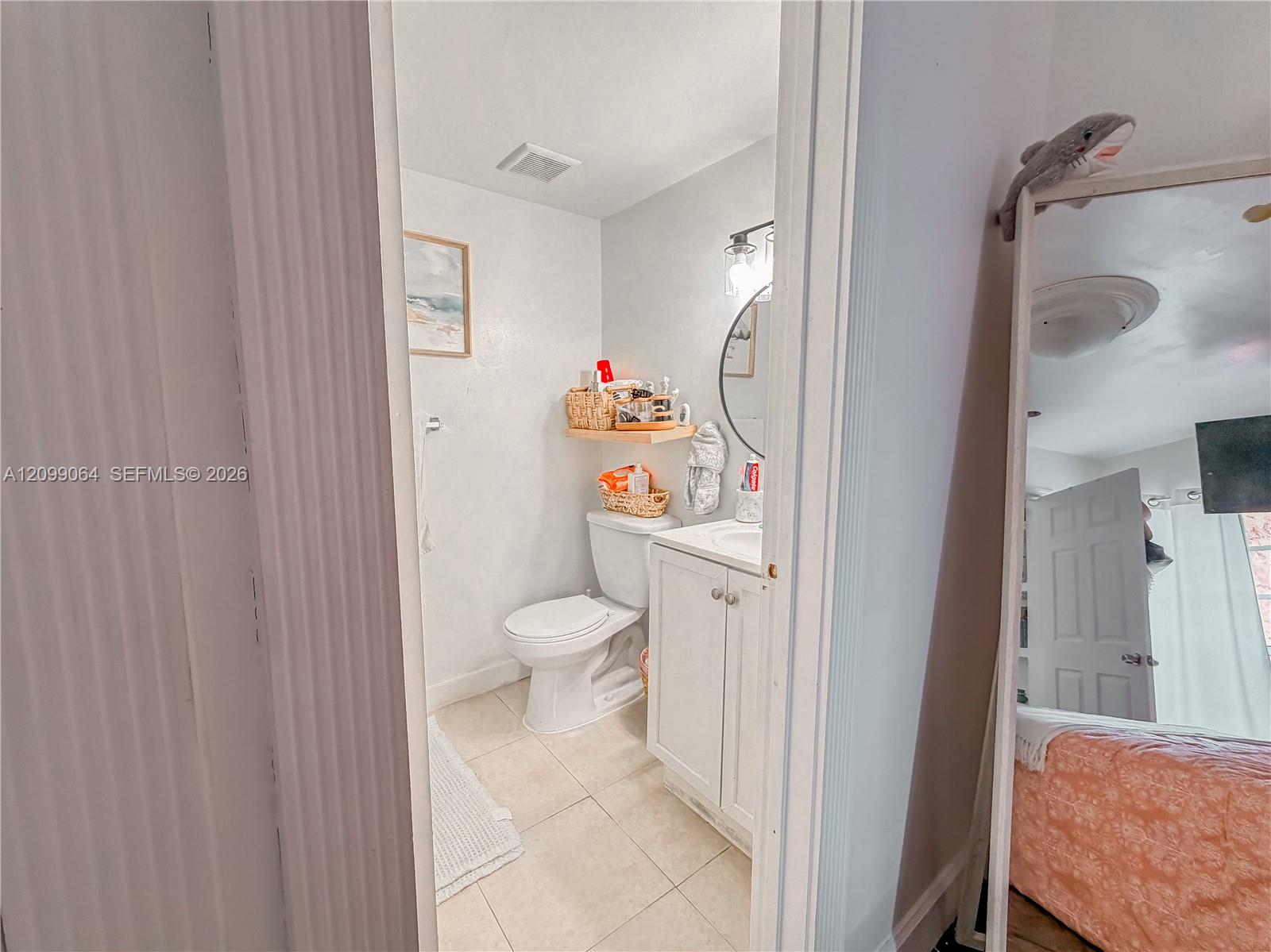 Bathroom with white toilet and vanity, beige tile floor, and round mirror.
