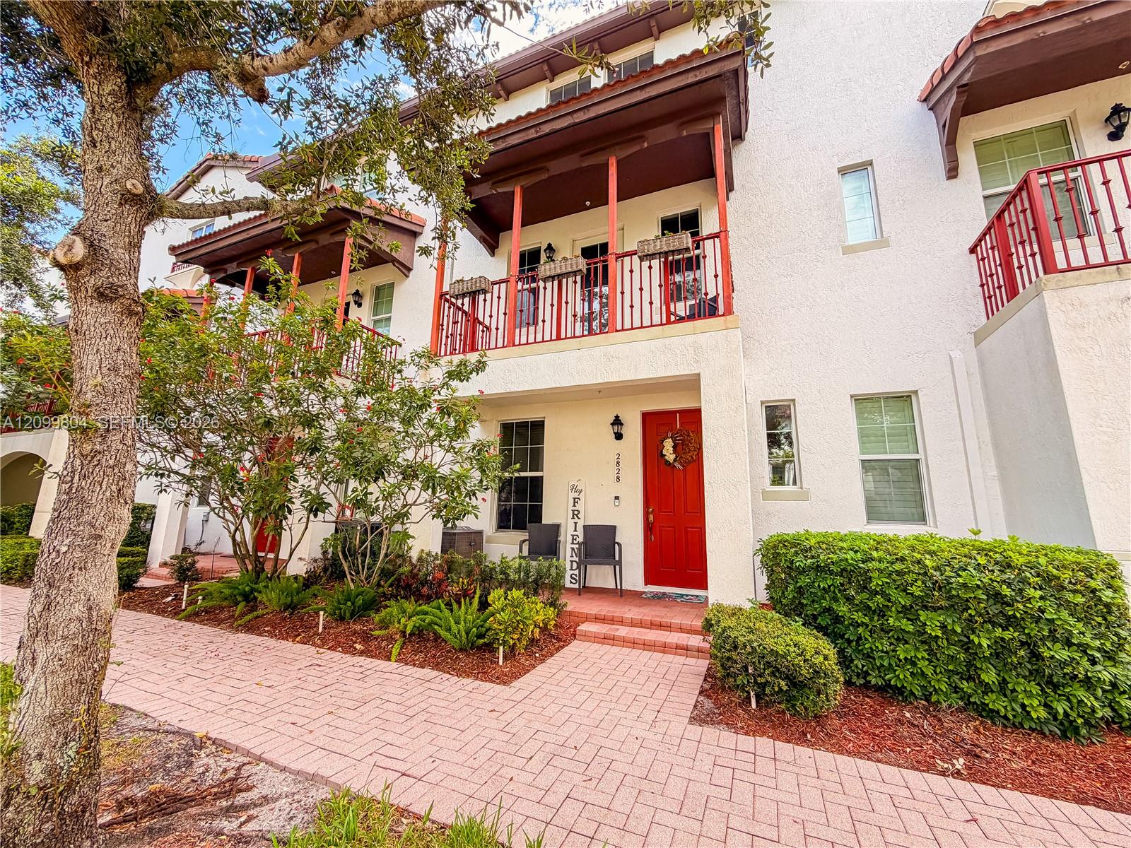 White two-story townhome with red balconies and a bright red front door beside a brick-paver walkway.