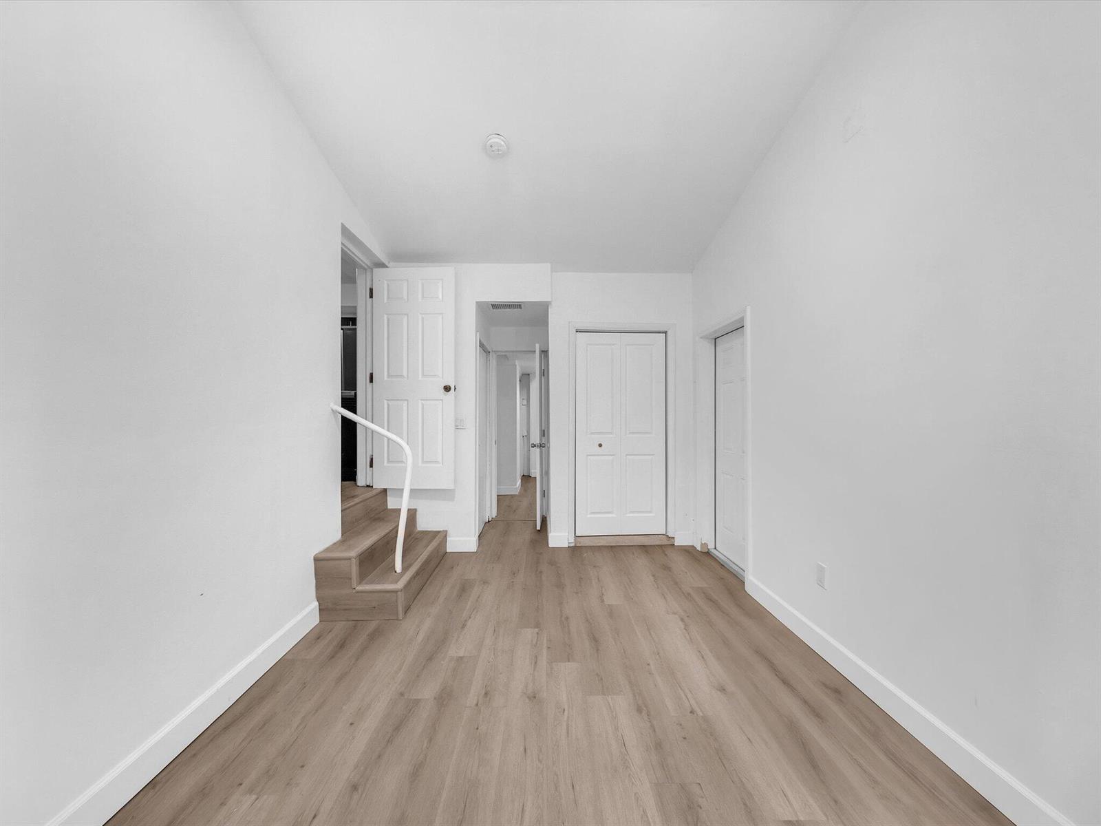 Empty hallway with light wood-look floors, paneled doors, and a short staircase.