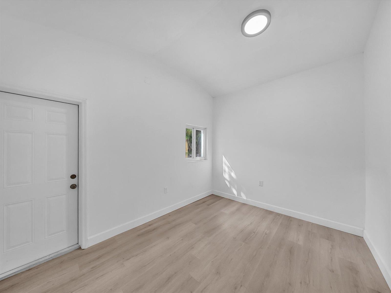 Empty room with light wood-look flooring, white walls, and a small window.