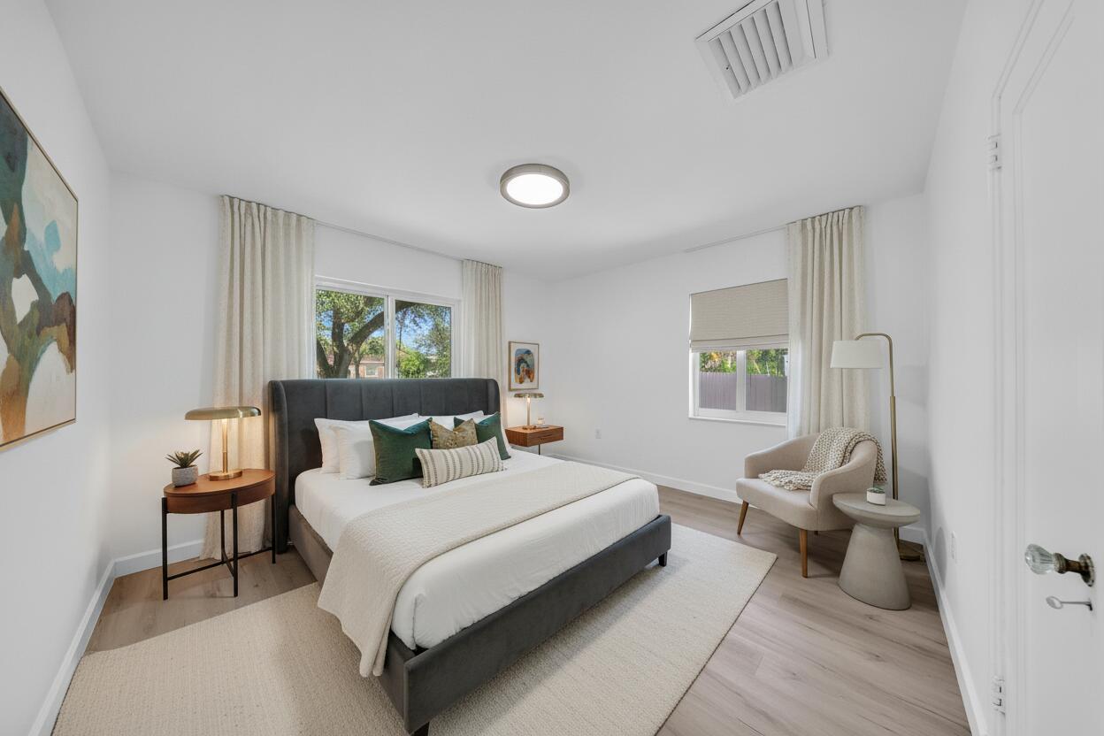 Staged bedroom with a charcoal bed, green accent pillows, light wood flooring, and a cream reading chair.