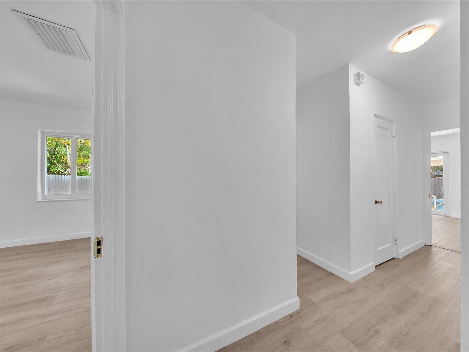 Vacant white hallway with light wood floors, adjoining rooms, and a glimpse of a pool.