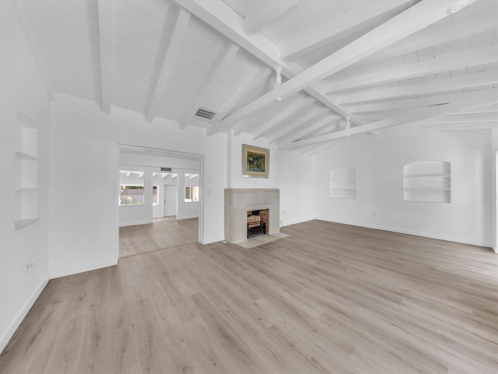 Living room with vaulted beam ceiling, fireplace, built-in shelves, and pale wood-look flooring.