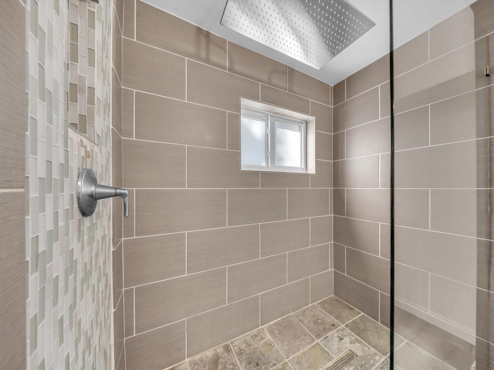 Walk-in shower with beige tile, a mosaic accent wall, rainfall showerhead, and small frosted window.