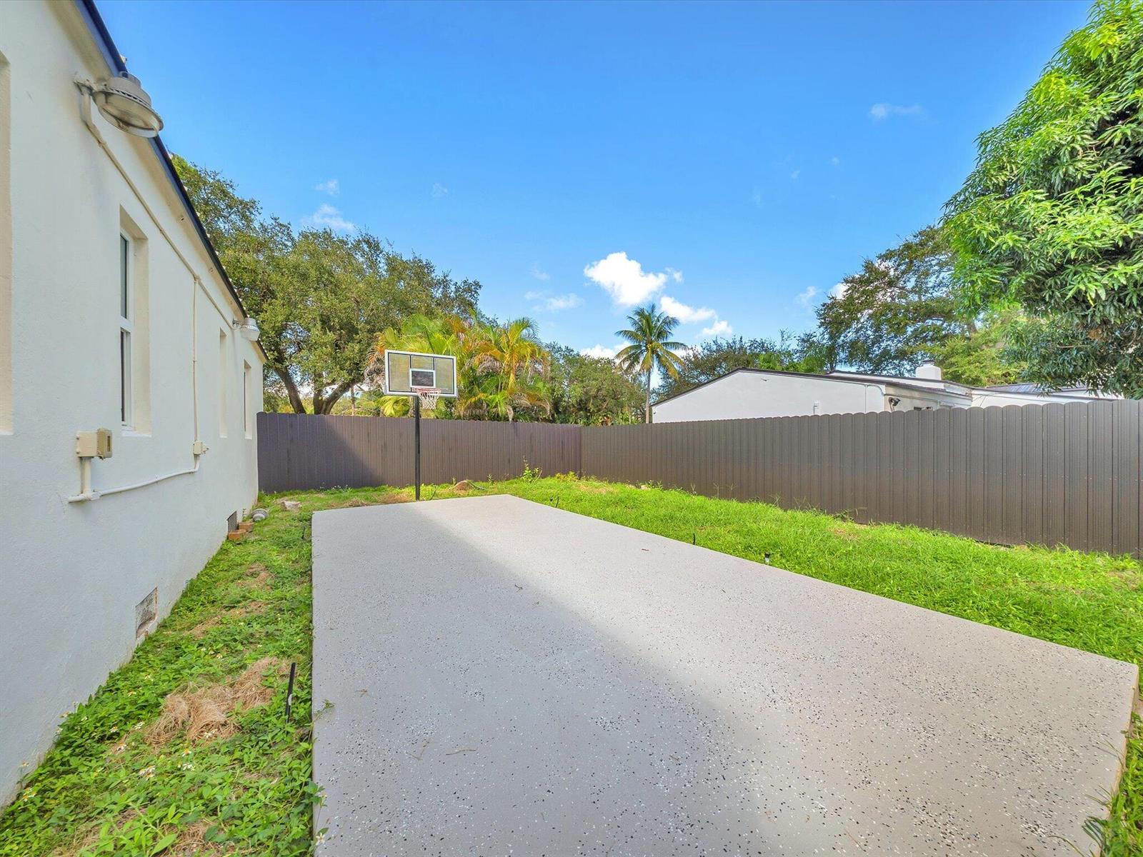 Backyard patio with a basketball hoop, lawn, and tall privacy fence.