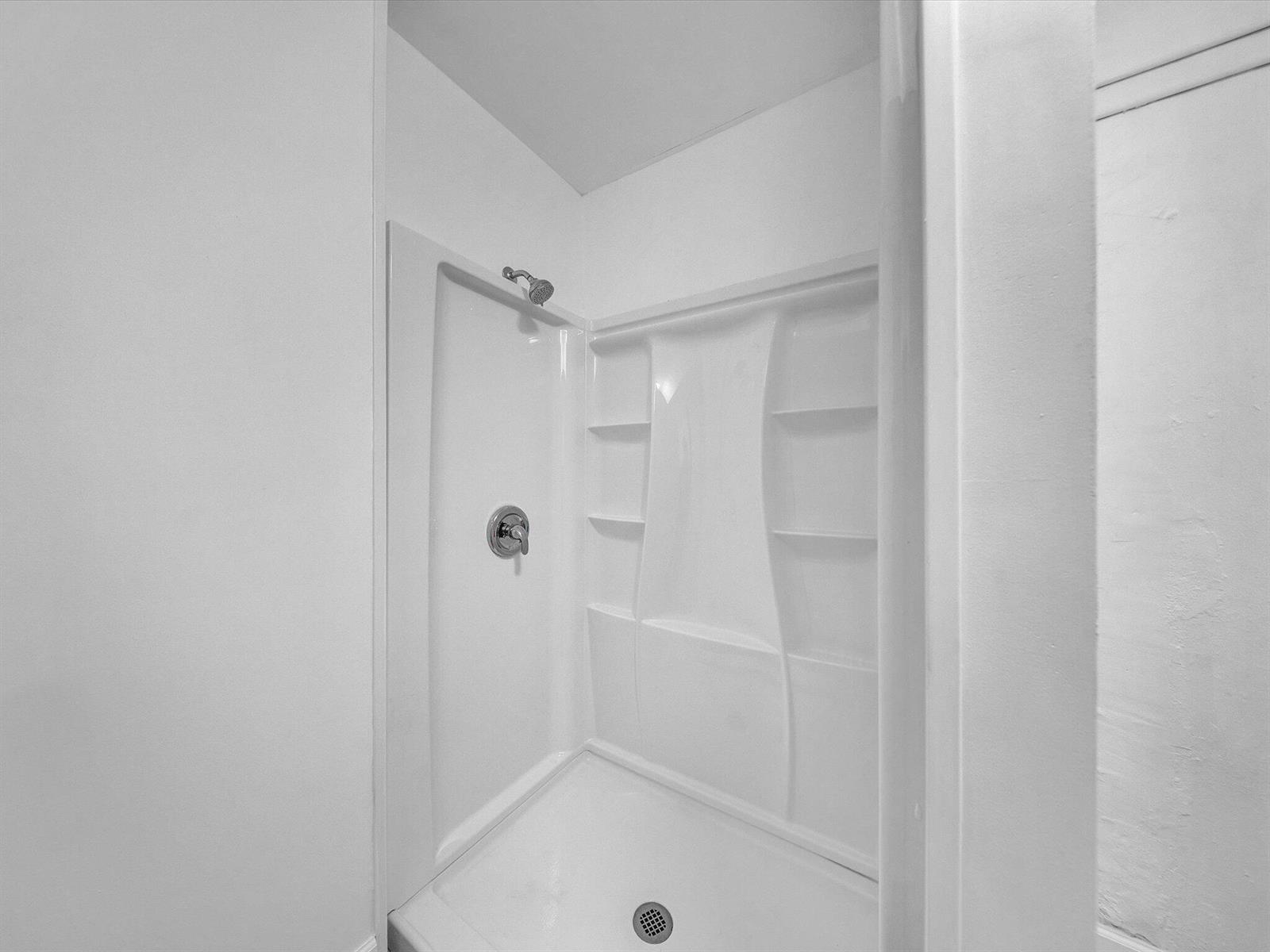 White walk-in shower with built-in shelves and chrome fixtures.