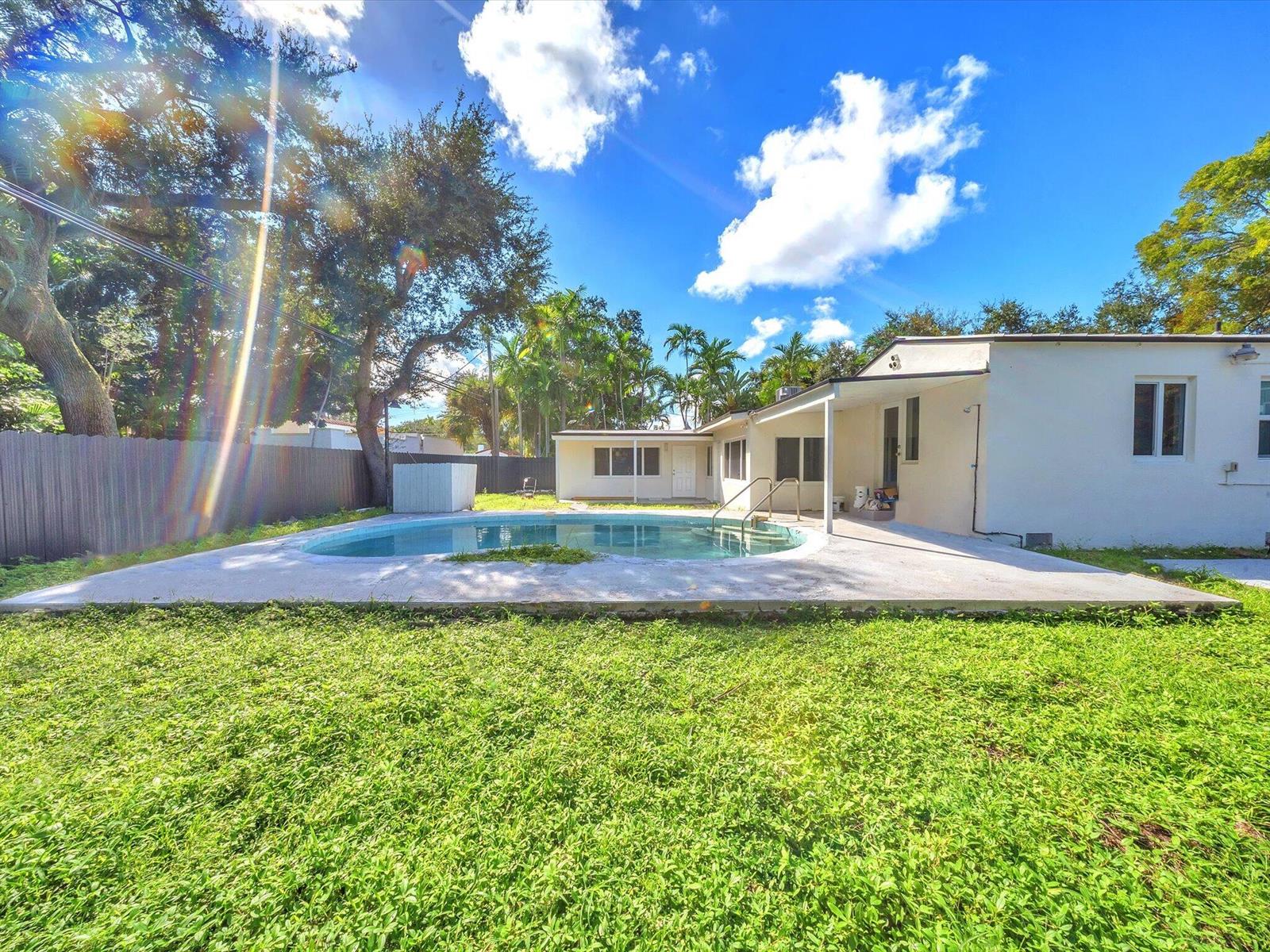 White house and curved backyard pool with a broad deck, lawn, and palms.