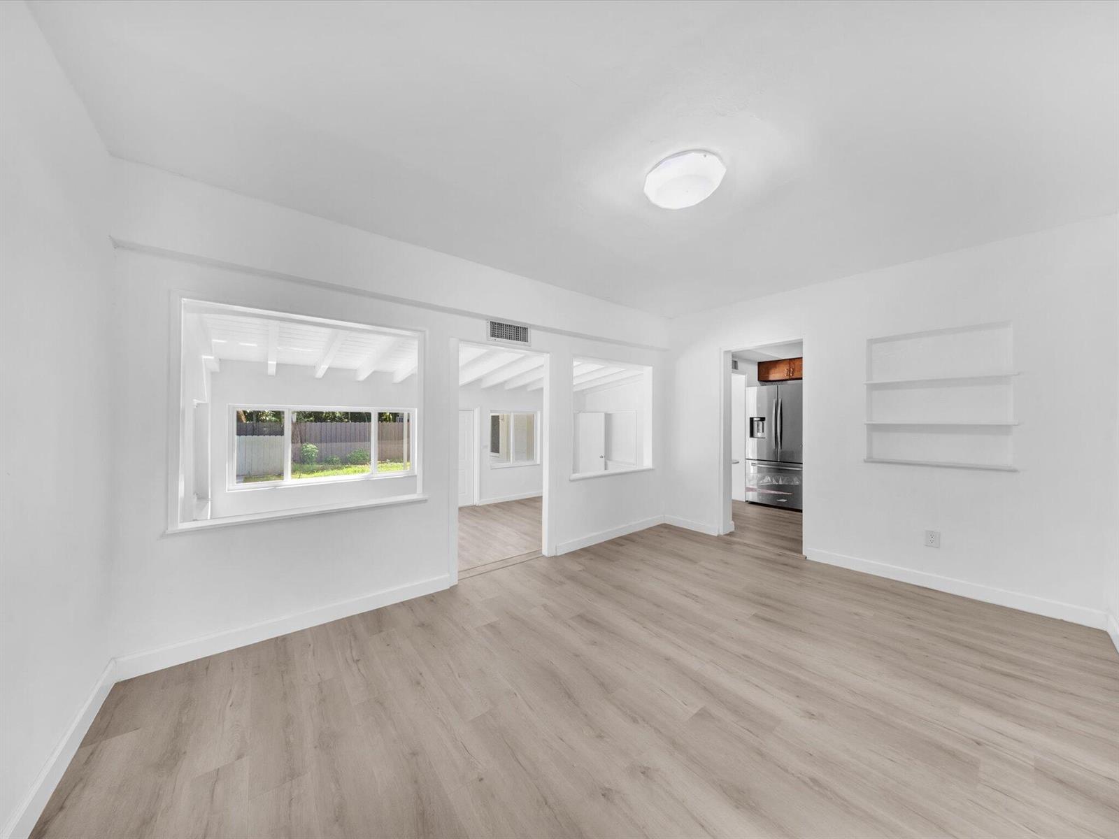 Empty living room with light wood-look floors, built-in shelves, and wide openings to adjoining rooms.