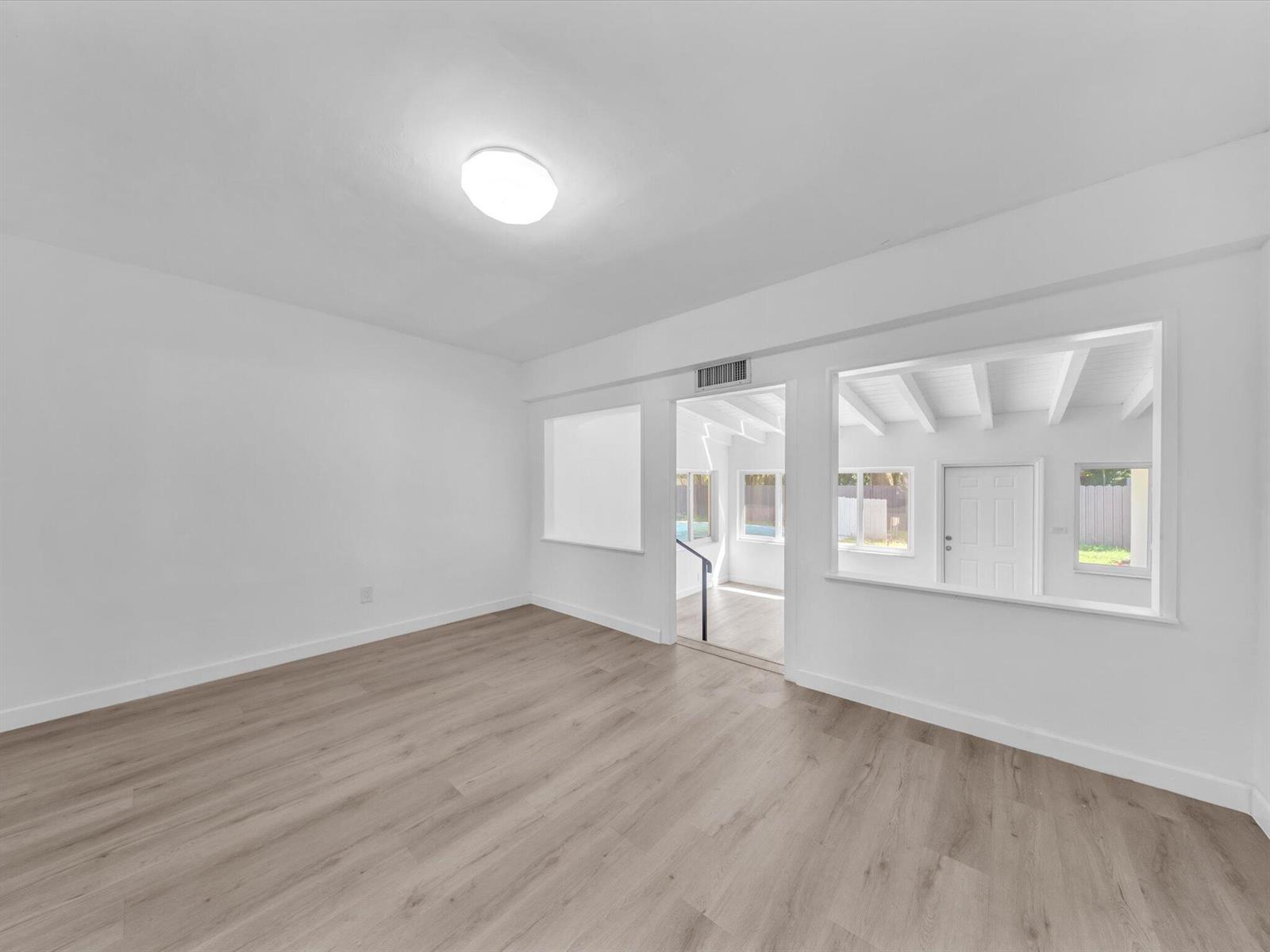 Empty interior room with light wood-look floors and a wide opening to a beamed room.