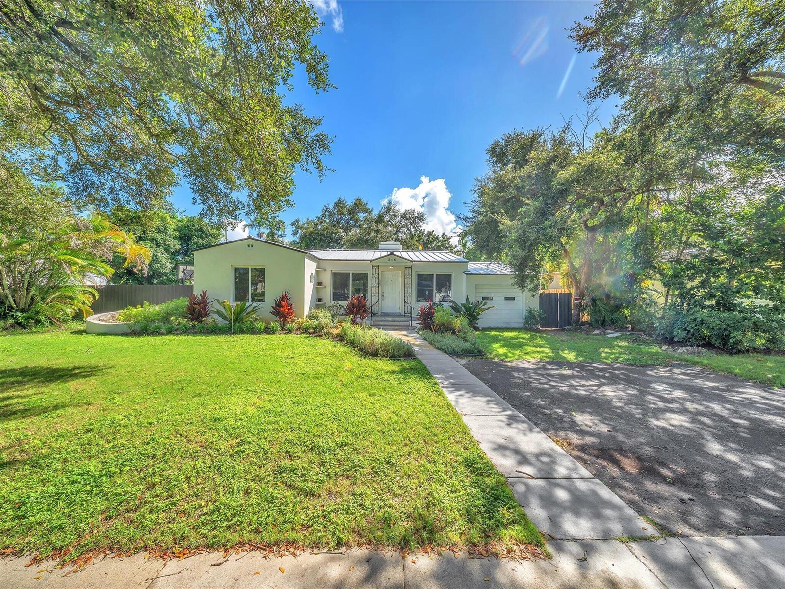 Single-story home with an attached garage, leafy trees, and a broad lawn.
