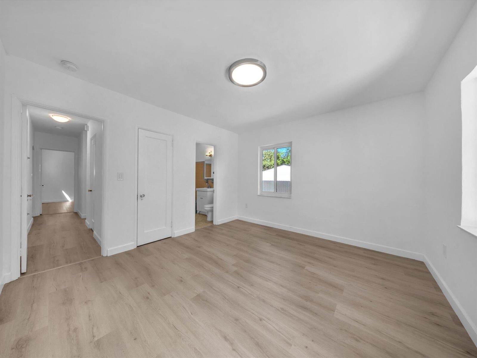 Vacant bedroom with light wood-look flooring, a window, and a doorway to the bathroom.