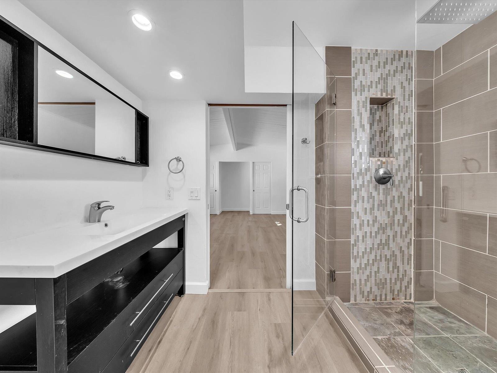 Bathroom with a dark floating vanity and glass shower featuring a vertical mosaic tile accent.