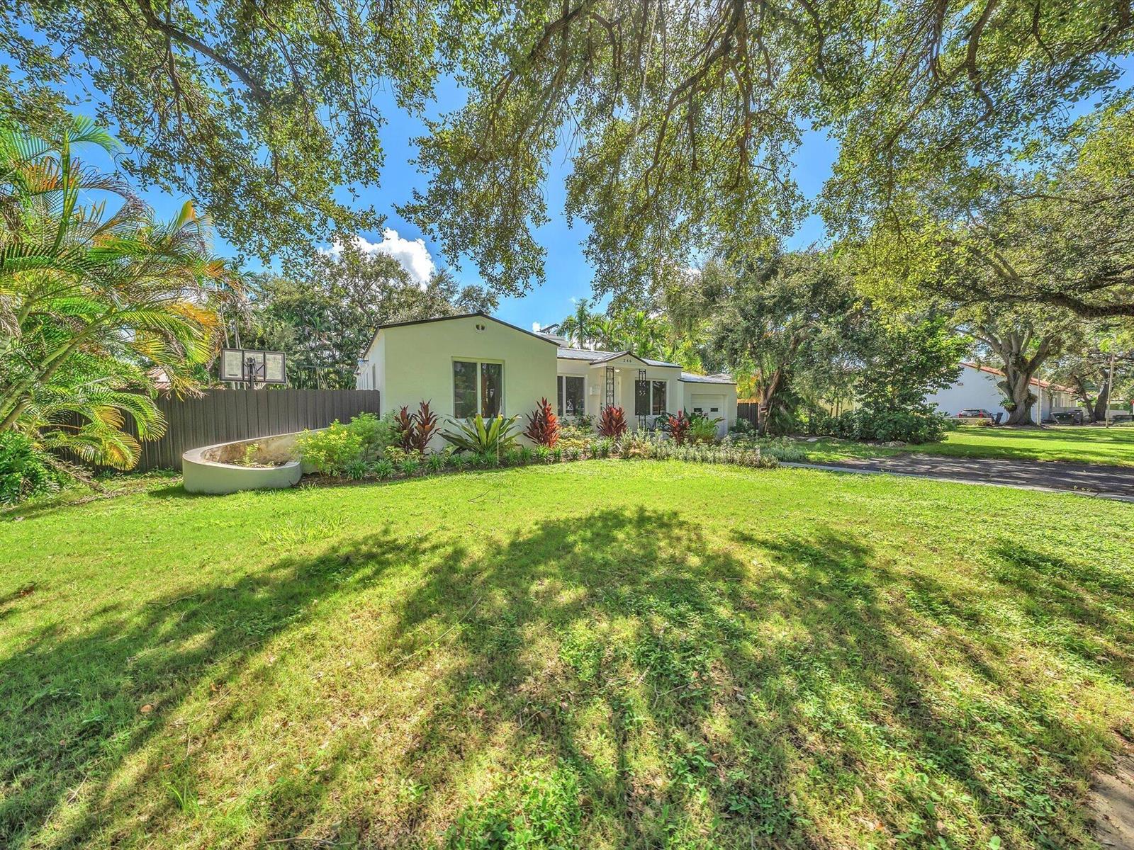 Single-story home behind a broad lawn, framed by mature trees and landscaped garden beds.