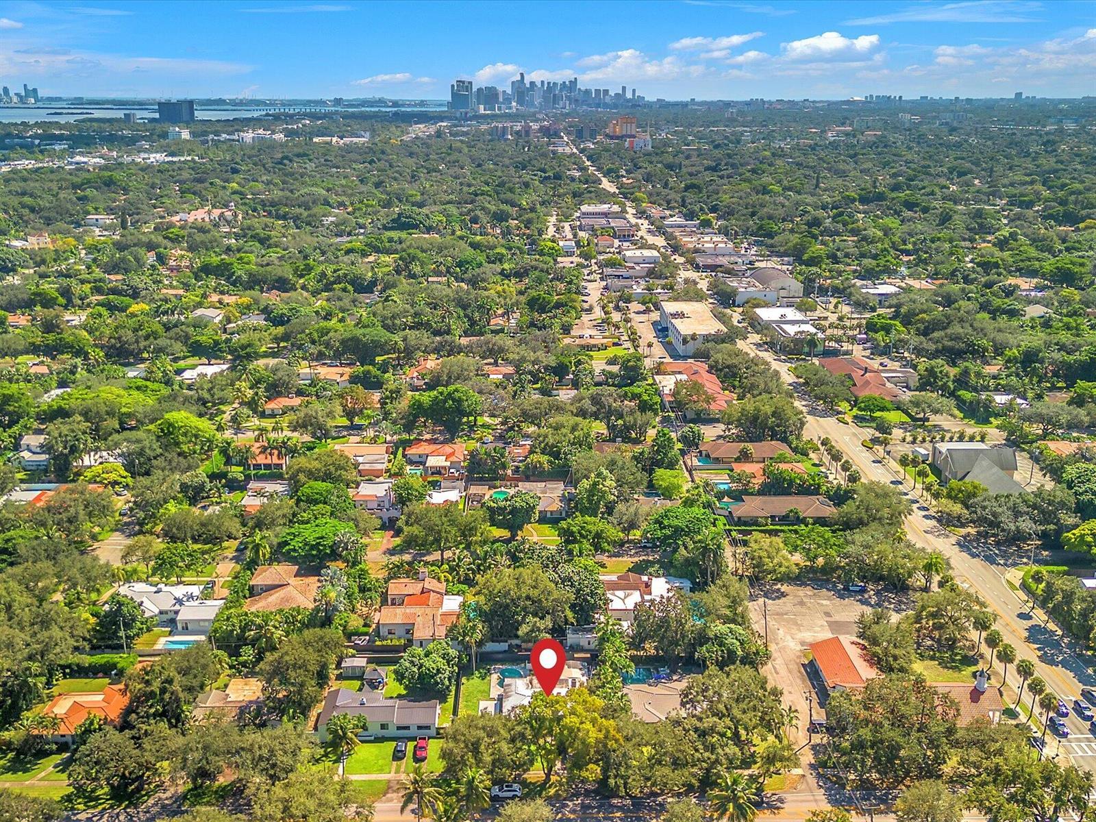 Aerial Miami Shores neighborhood with a marked home, tree canopy, and distant downtown skyline.