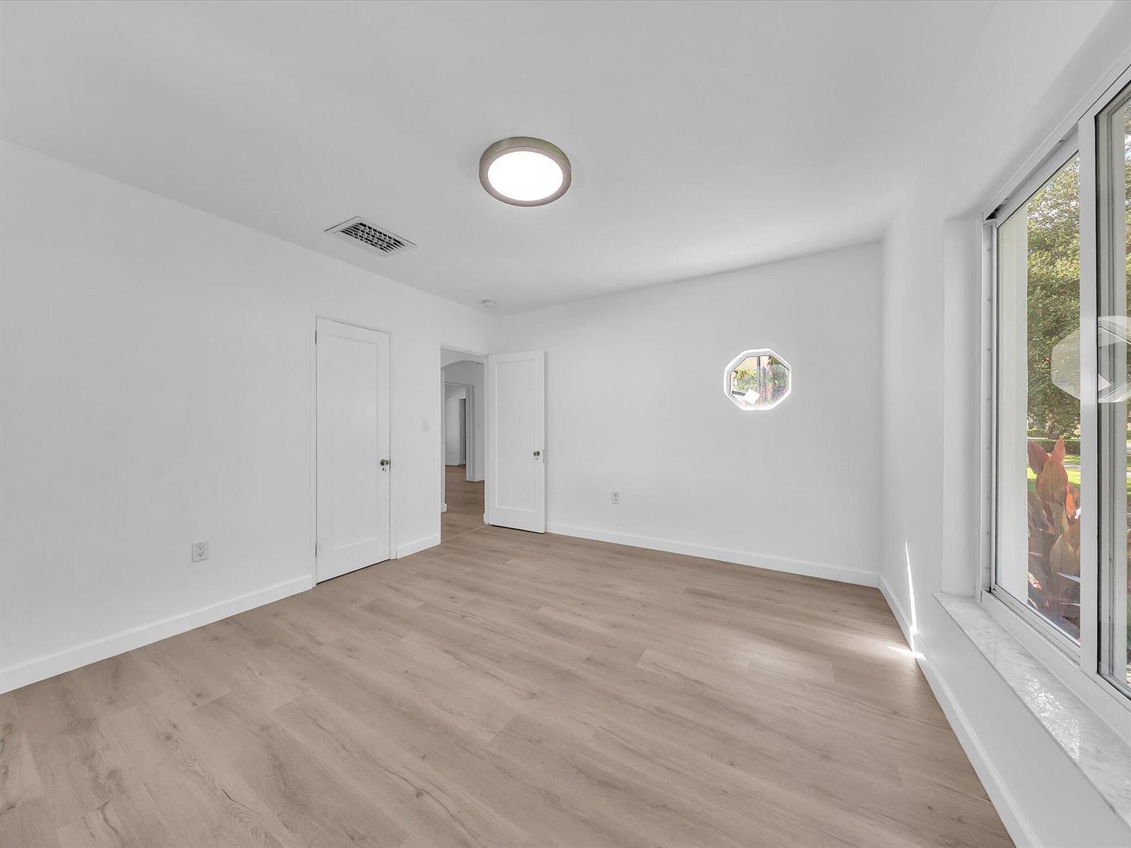 Empty room with light wood-look floors, an octagonal window, and large windows overlooking greenery.