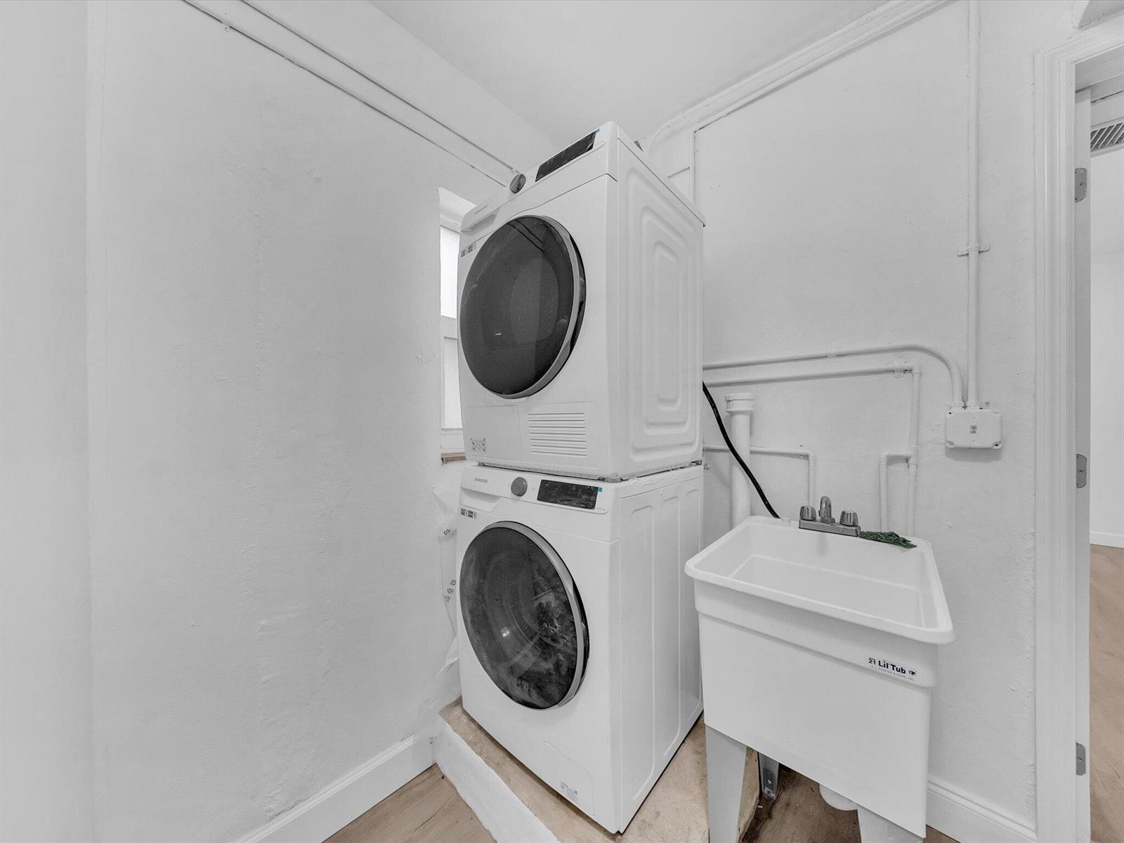 Laundry area with stacked front-loading washer and dryer beside a deep utility sink.